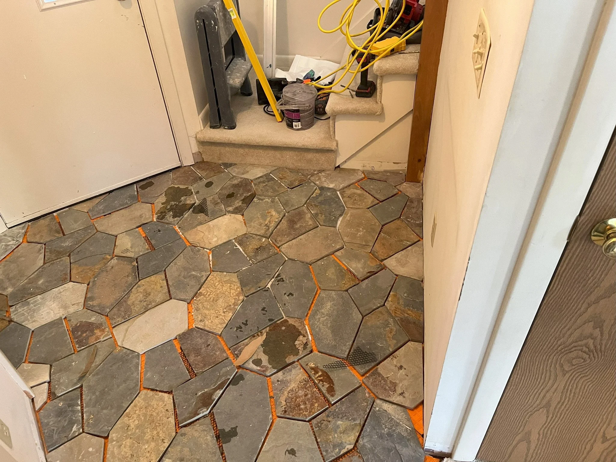 Indoor space with a stone tile floor, cluttered staircase with construction tools, cables, a bucket, and a small ladder.