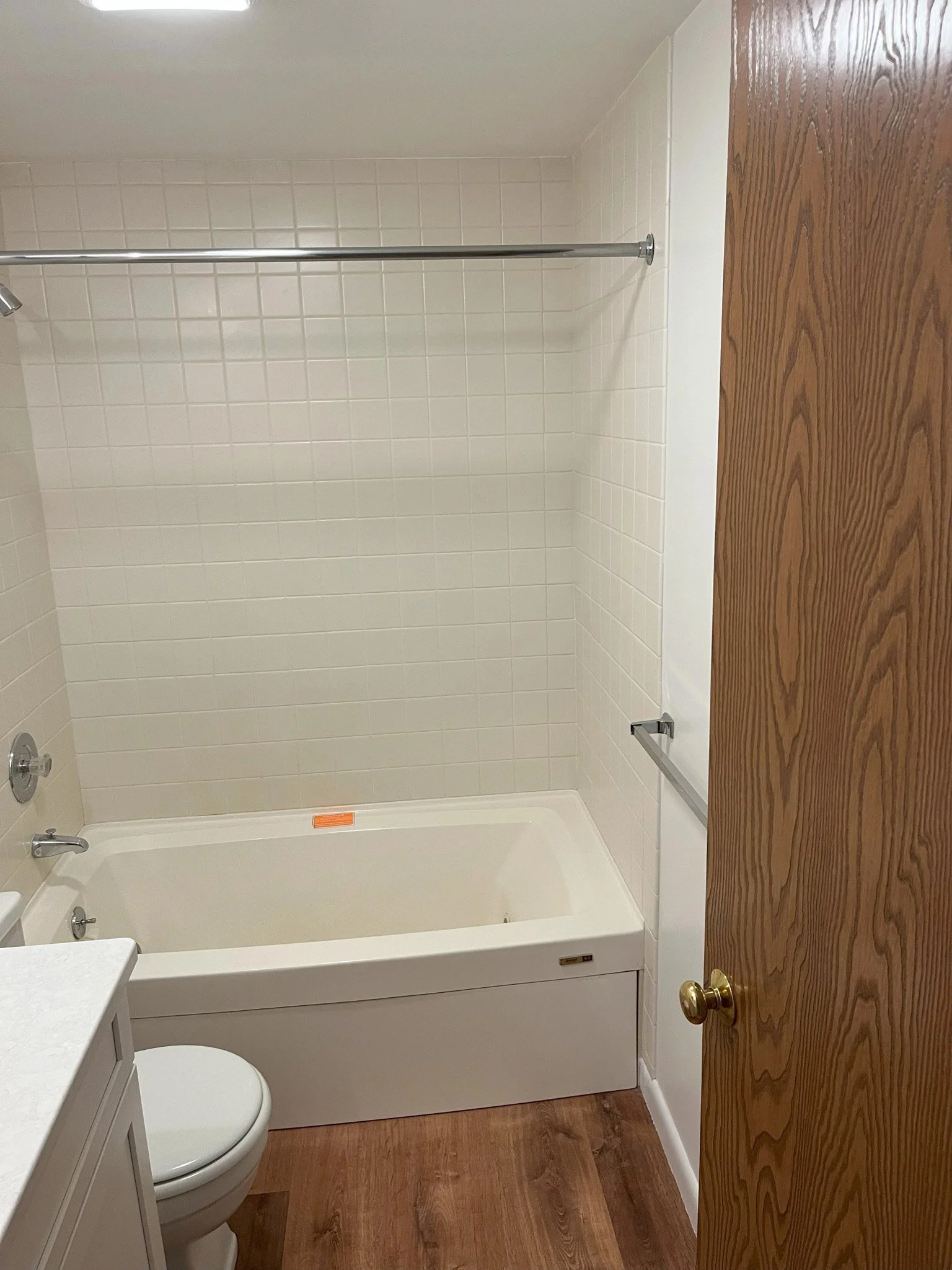 Bathroom with bathtub, toilet, wooden door, white tiled walls, and wooden flooring.