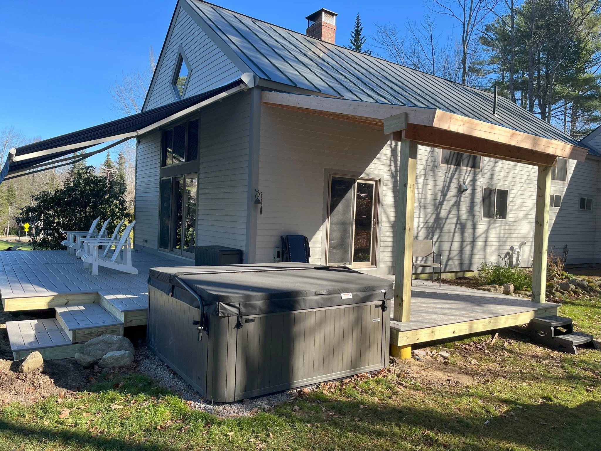 Backyard view of a house with a newly built wooden deck, a hot tub, and outdoor seating, under a clear blue sky.