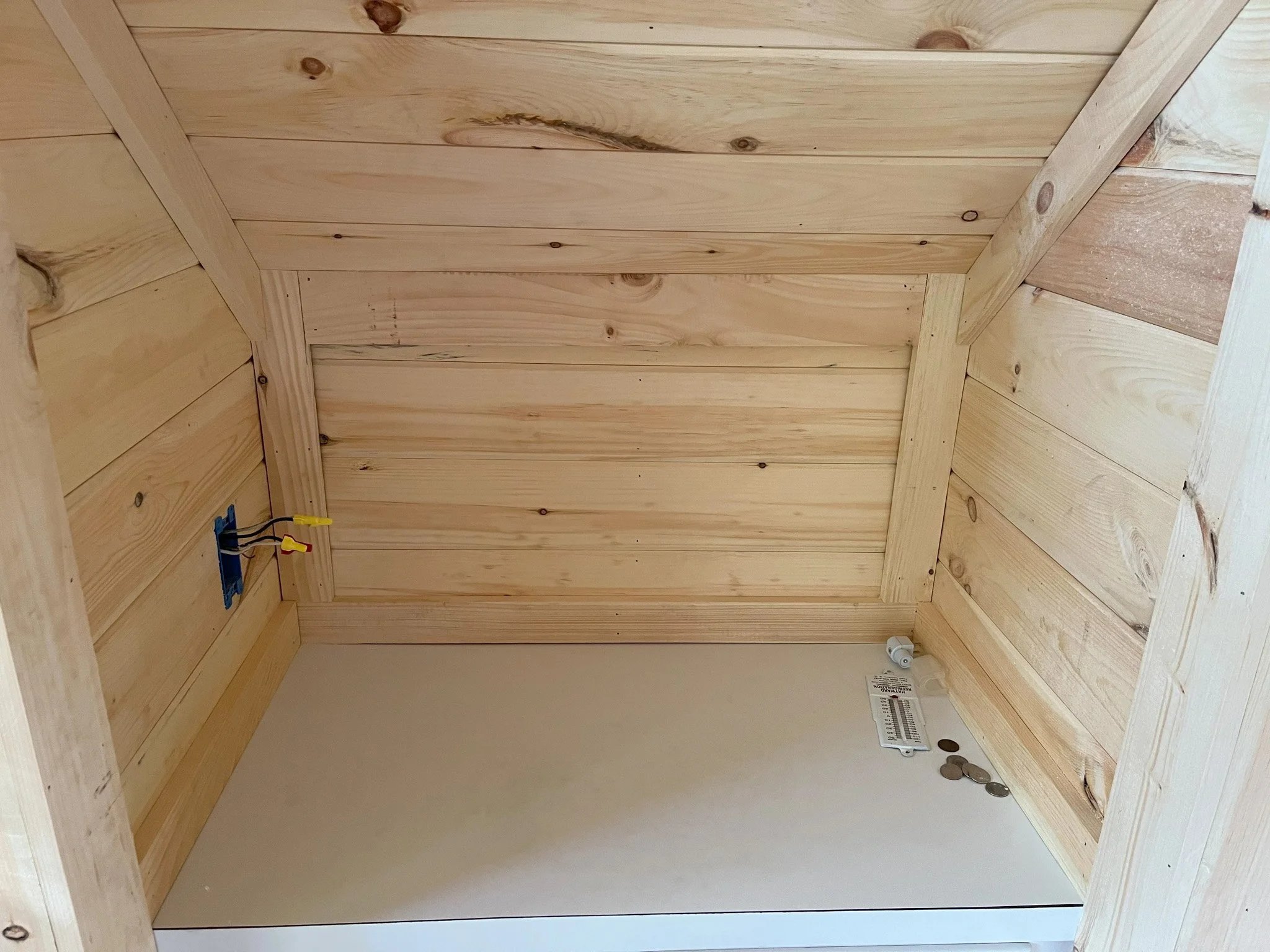 Interior view of a wooden room with unfinished wood walls and ceiling, electrical wiring, and a few coins on the floor.