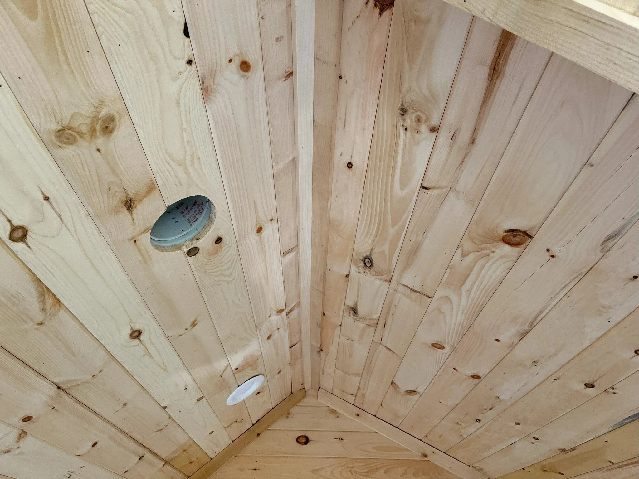 Wooden ceiling with a smoke detector, a recessed light, and an exhaust vent.