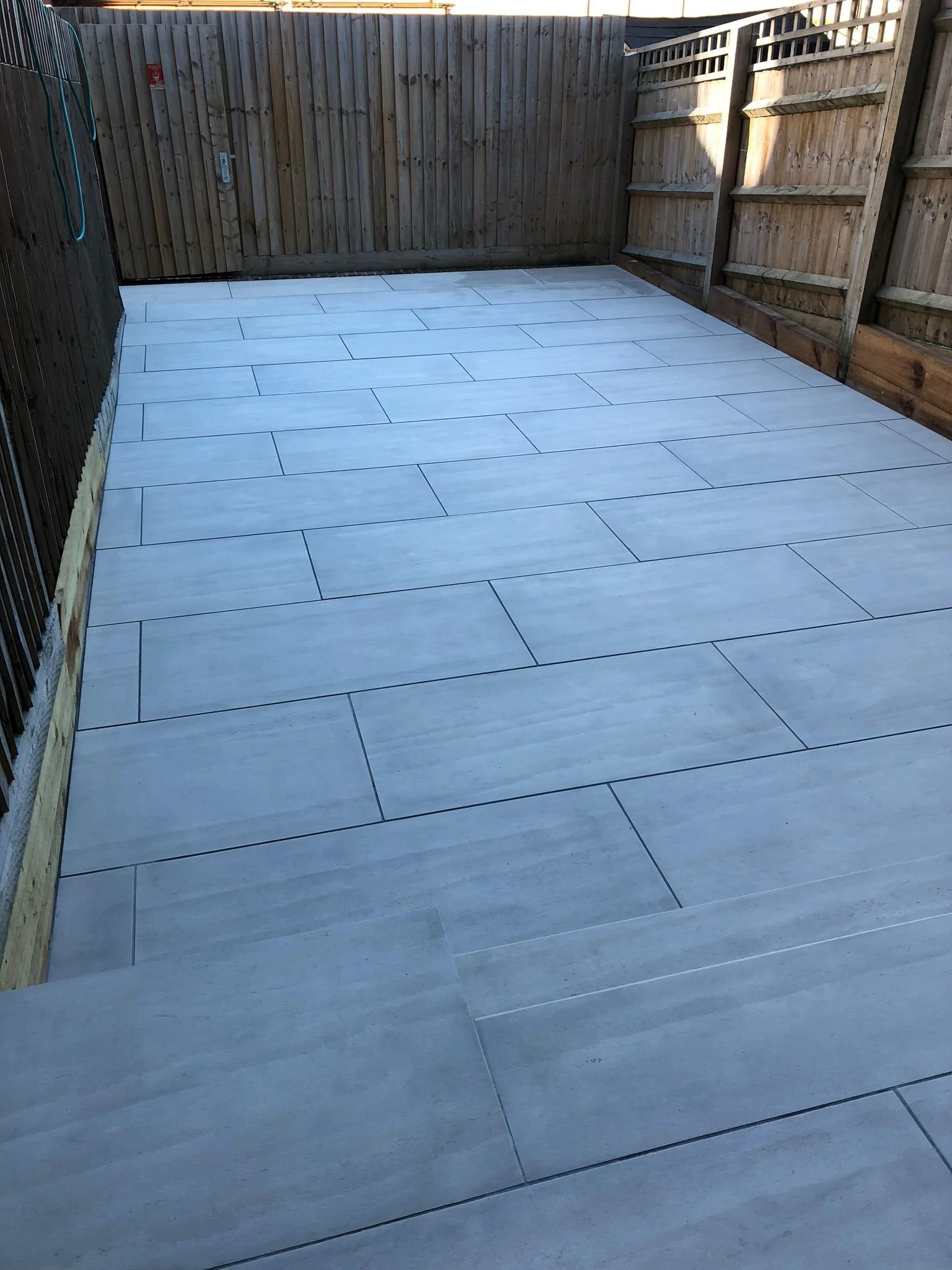Empty outdoor patio with new light-colored tile flooring enclosed by wooden fence panels.