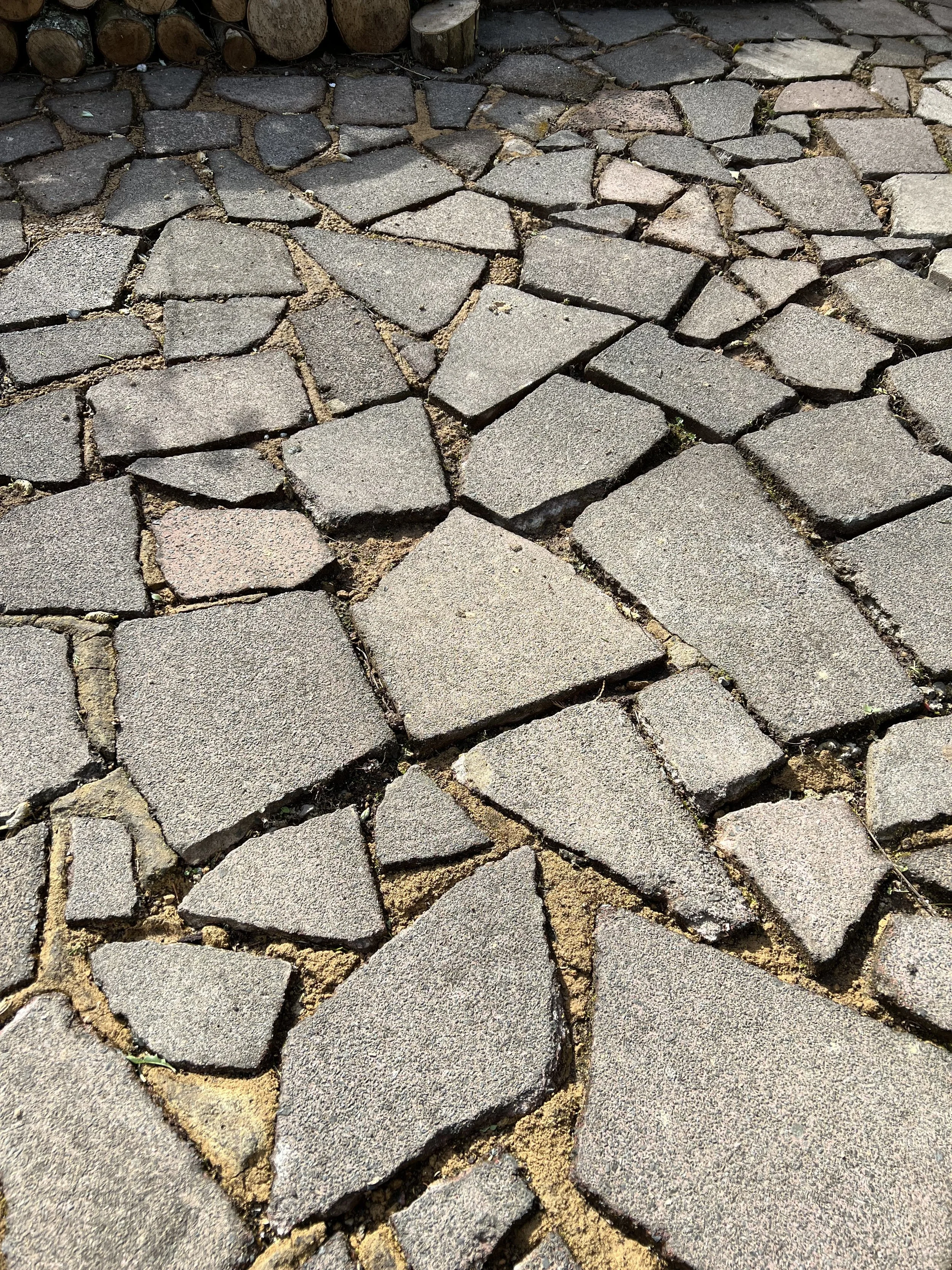 Close-up of uneven cobblestone pavement with gaps filled with dirt and small plants.