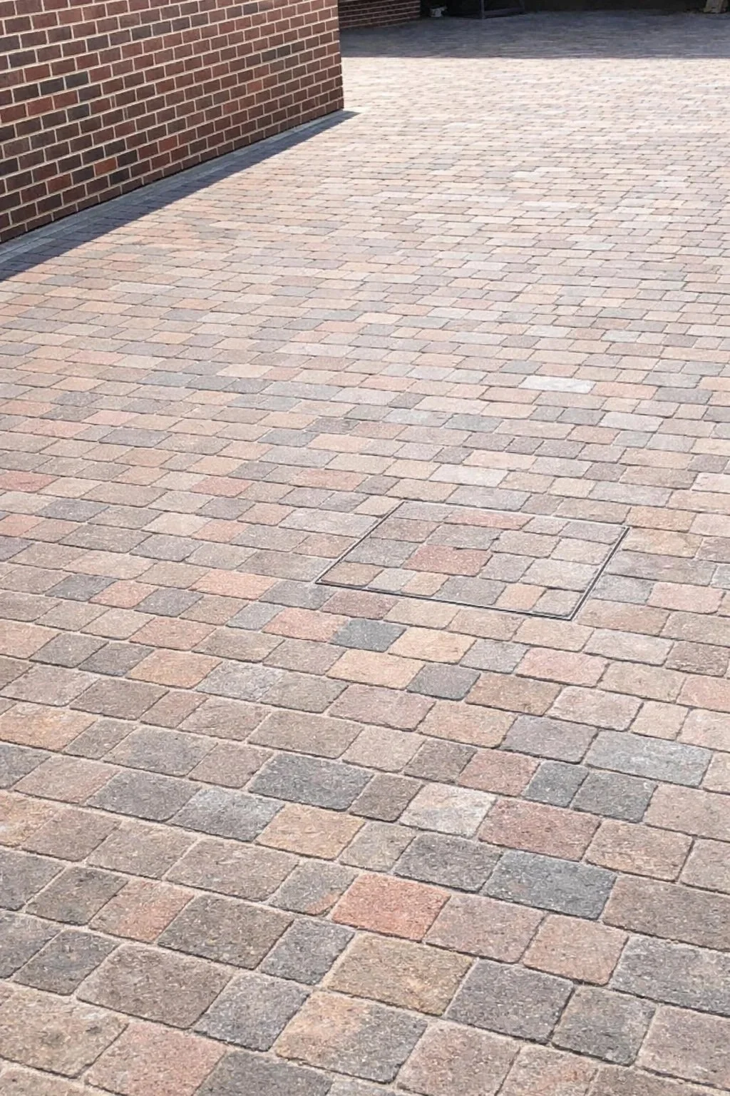 A paved brick driveway with a metal access hatch in the center and a brick wall on the left side.