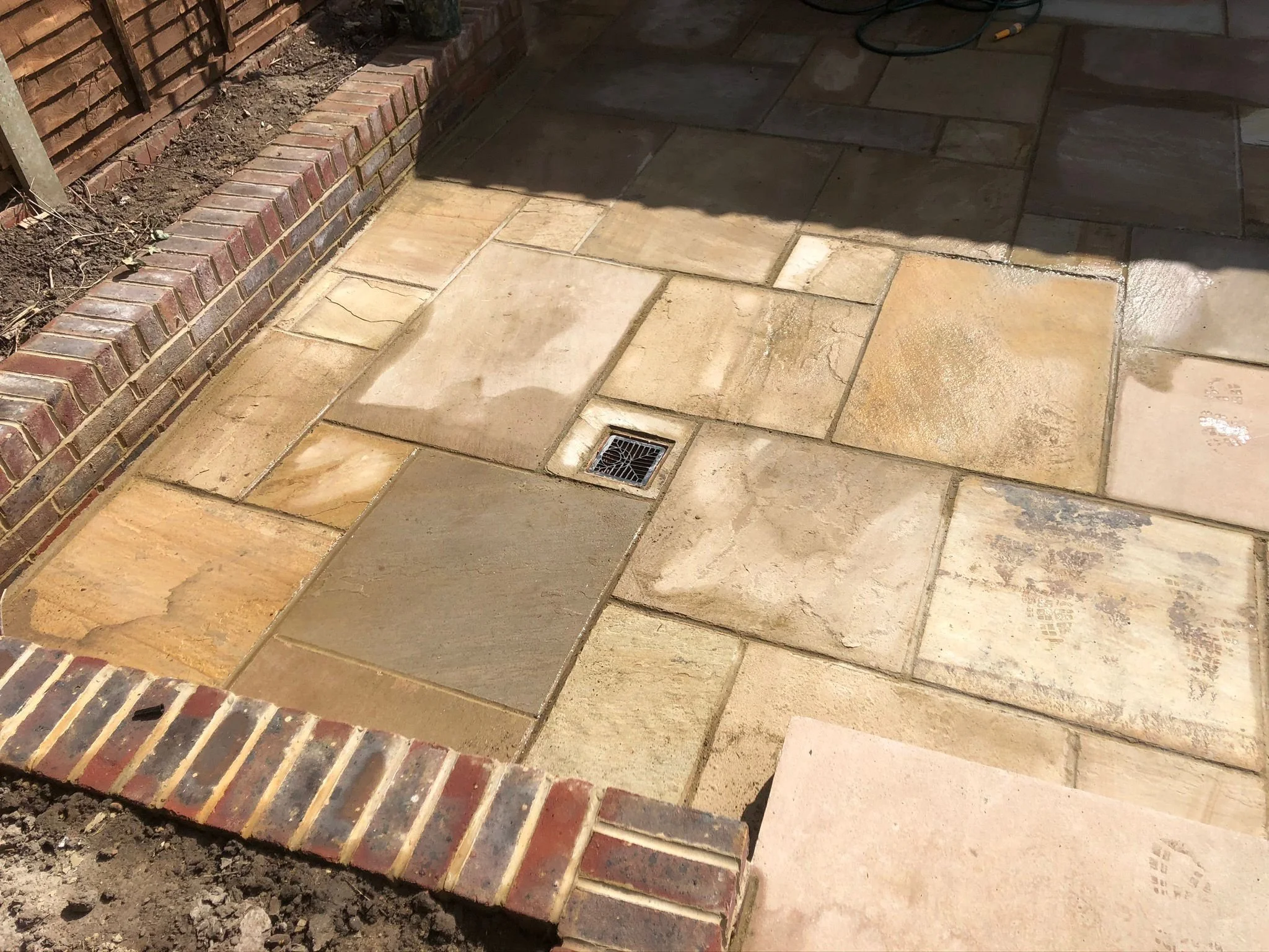 Newly installed rectangular stone patio with a central drain and brick border surrounding the stones.