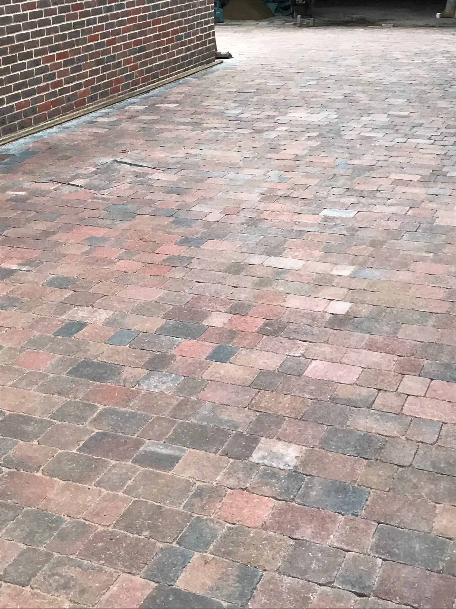 A brick-paved outdoor area with a brick wall on the left and a partially visible garage or storage space in the background.