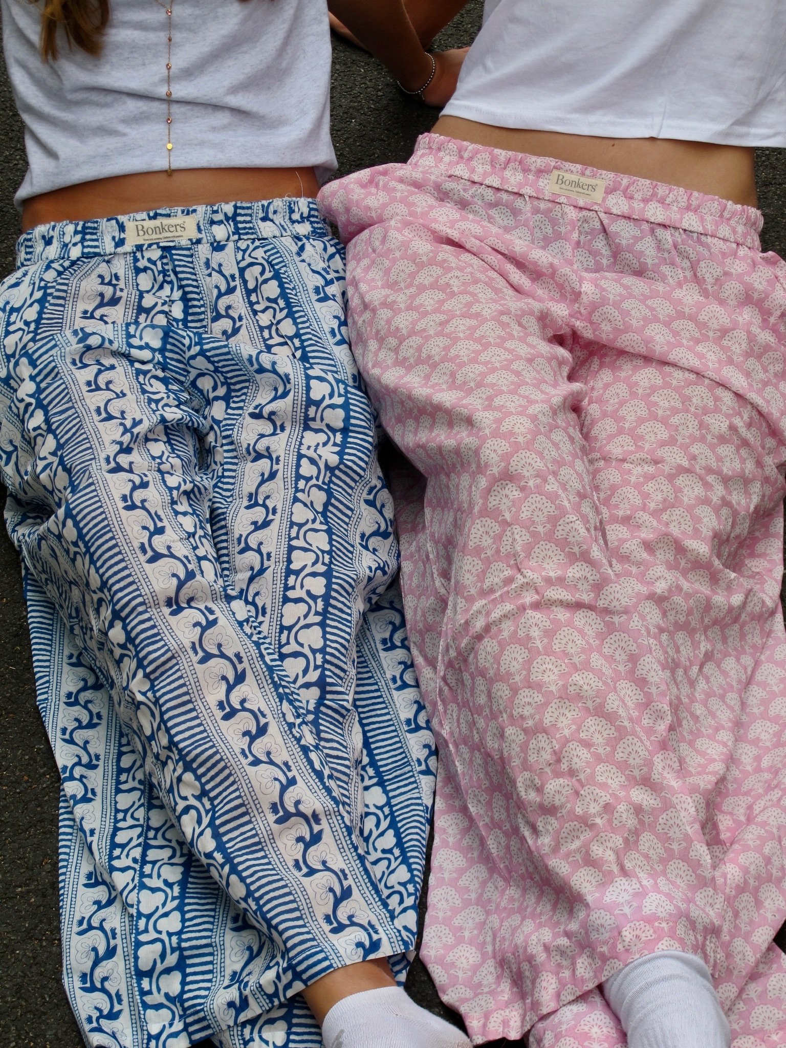 Two young women wearing casual clothing with pink and turquoise patterns, standing in front of a mint green door, smiling and posing playfully.