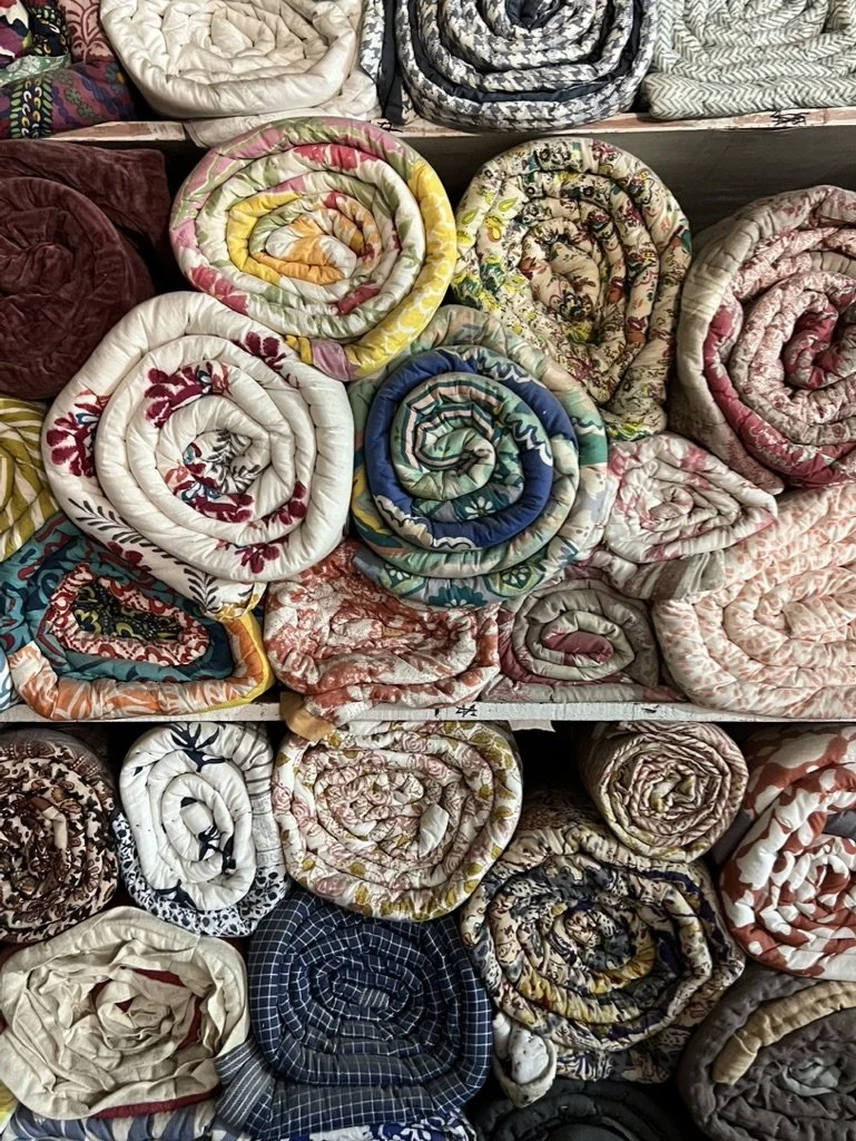 Stacked and rolled quilted blankets with various floral and patterned designs.