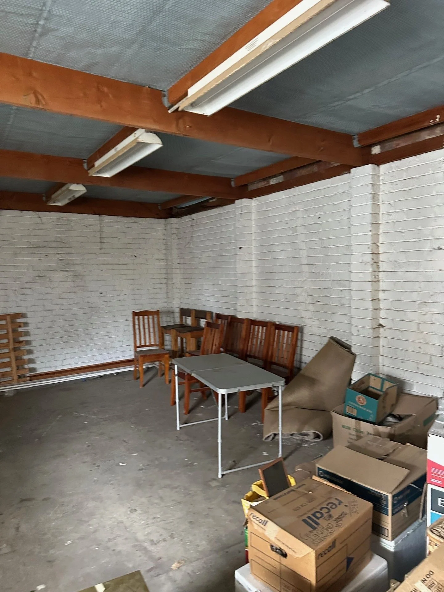 Photo of the existing garage interior with painted brick walls, exposed timber beams and a concrete floor before the conversion.