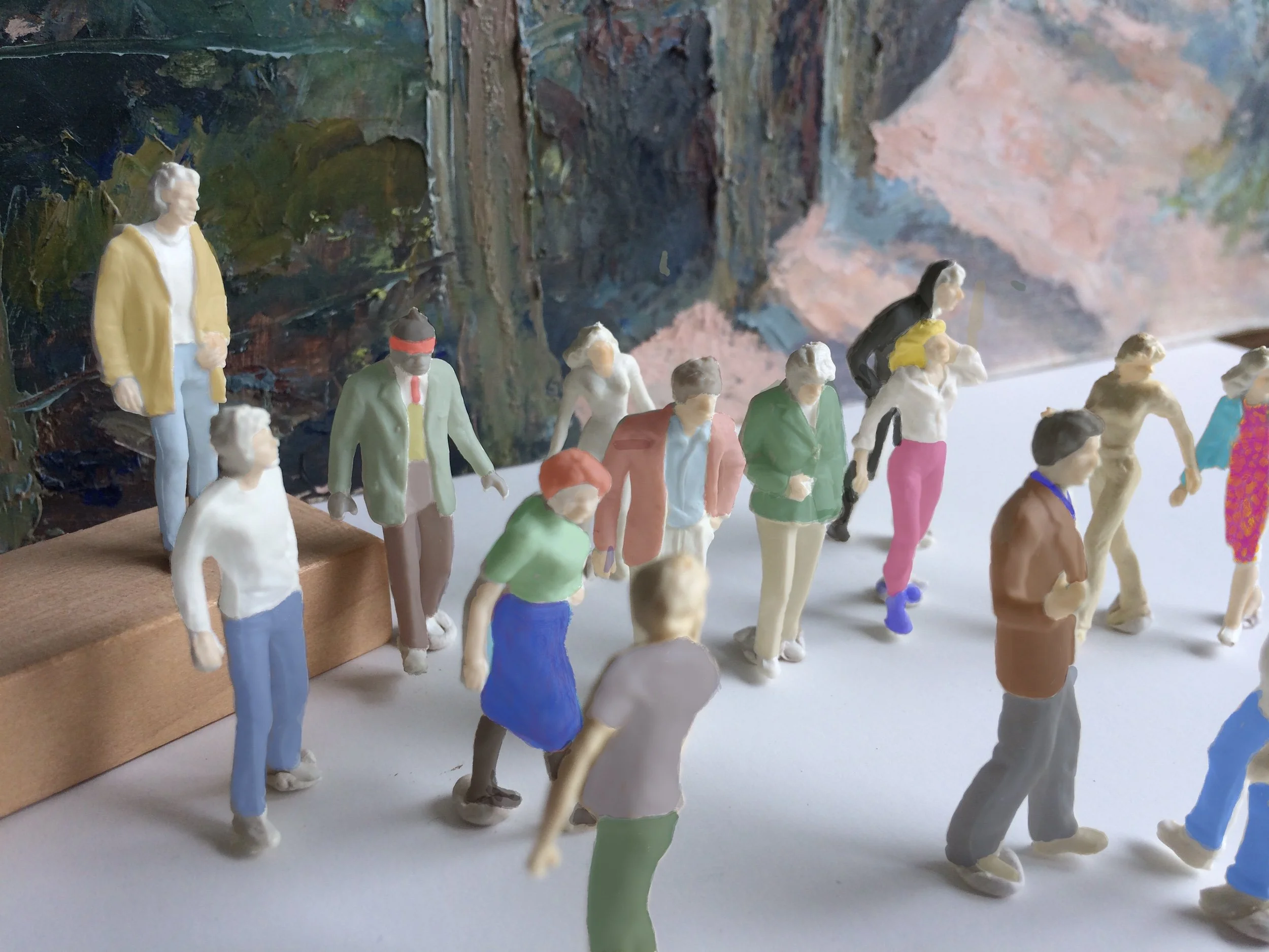 Miniature figurines of people standing and walking on a white surface, with a painted background.