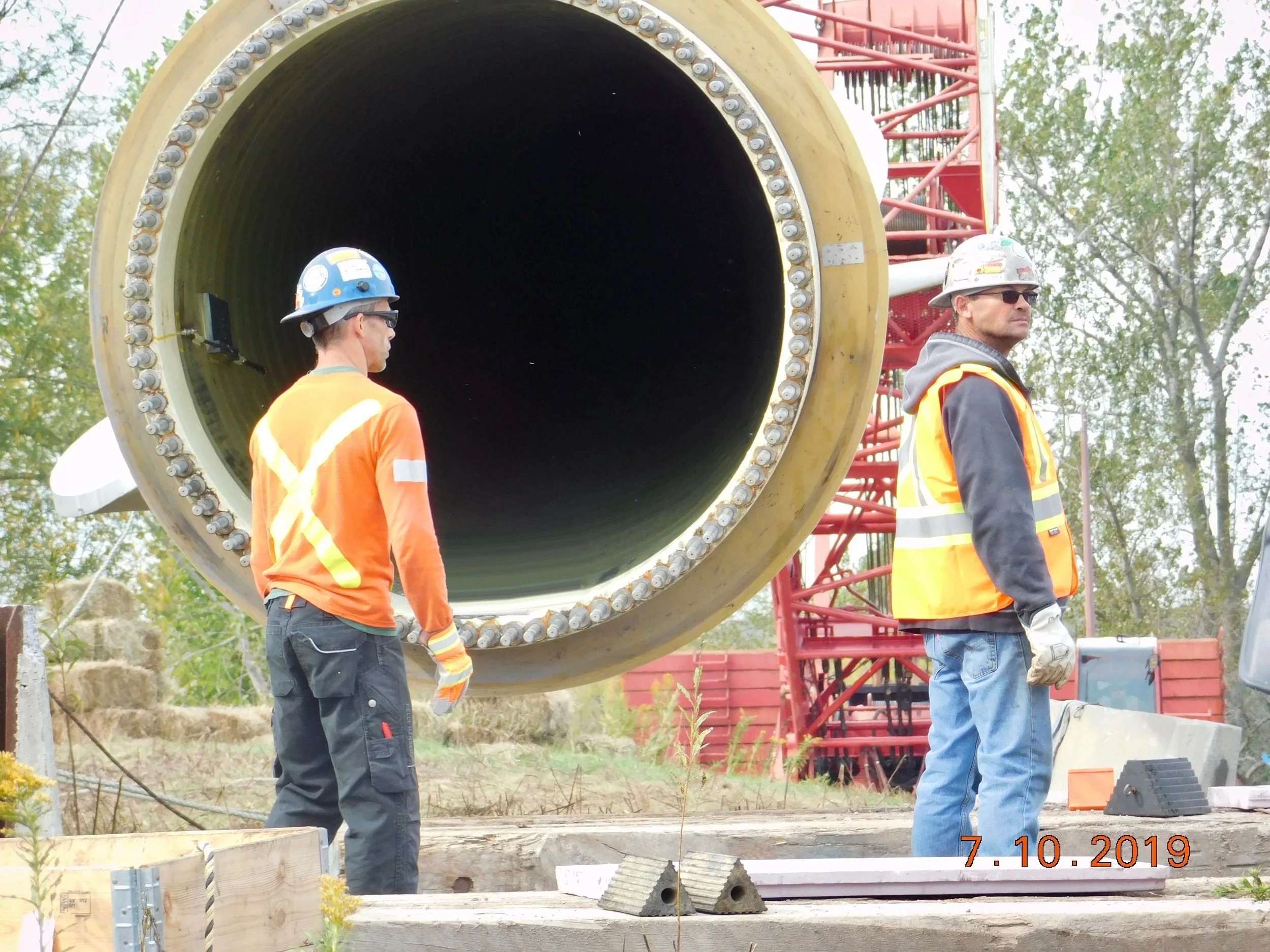 Crew in hard hats, safety glasses and hi-vis beside a wind turbine tower section