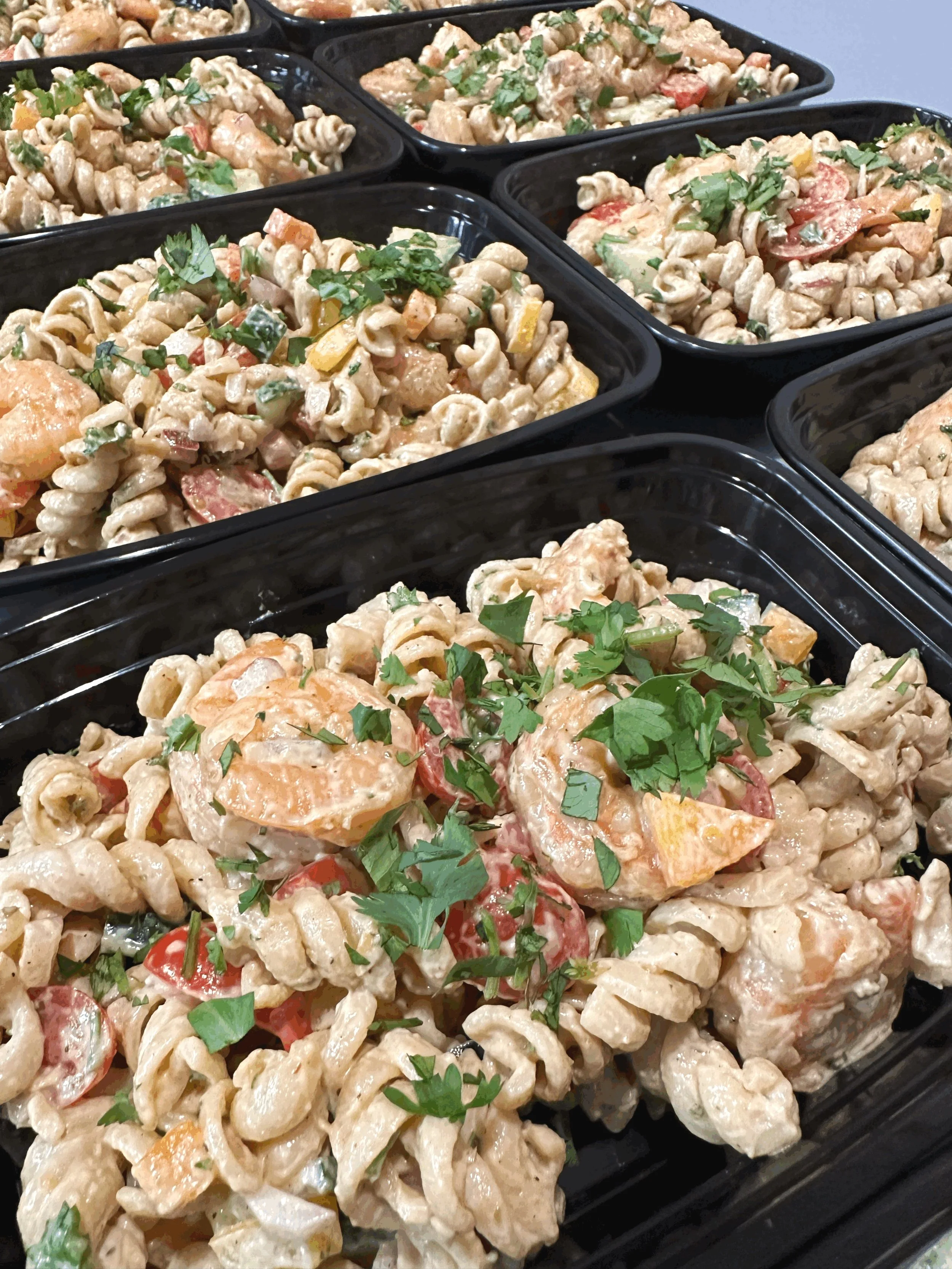 Meal prep containers filled with grilled chicken, roasted zucchini, pasta, and green onions.