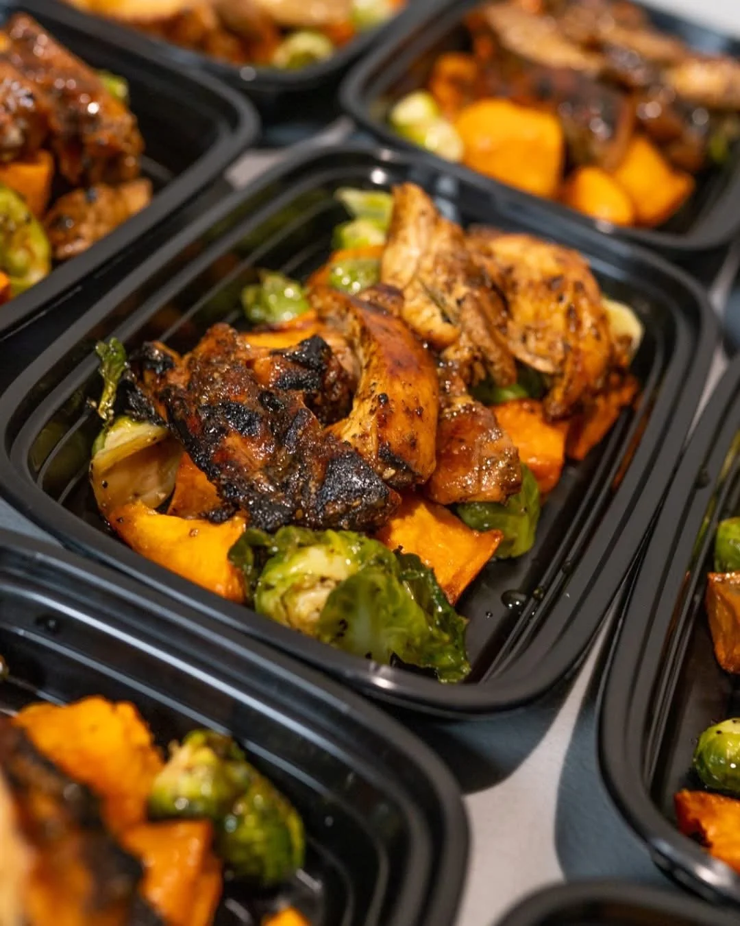 Meal prep containers filled with grilled chicken, roasted zucchini, pasta, and green onions.