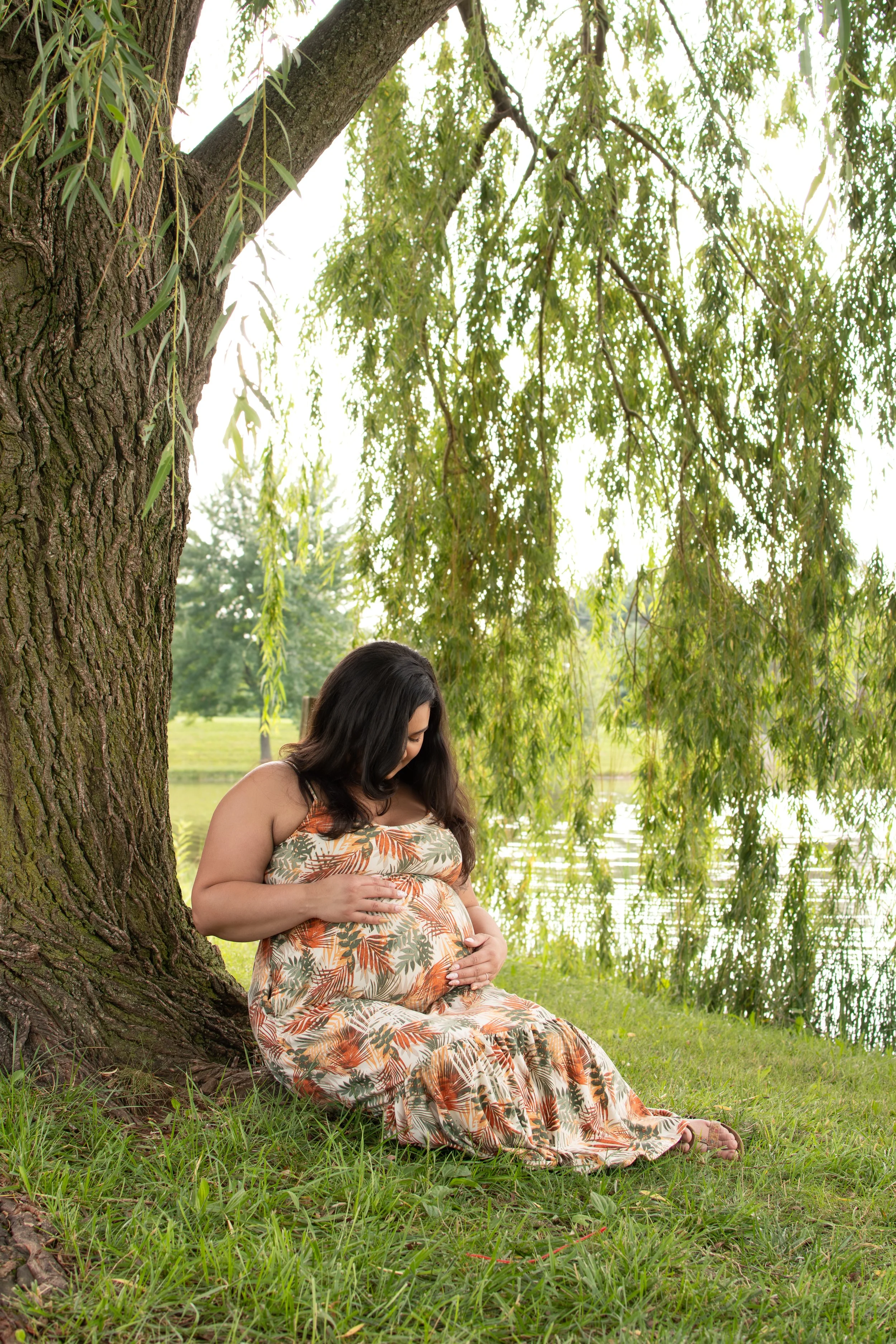 earthy maternity shoot beneath a weeping willow tree that is lakeside