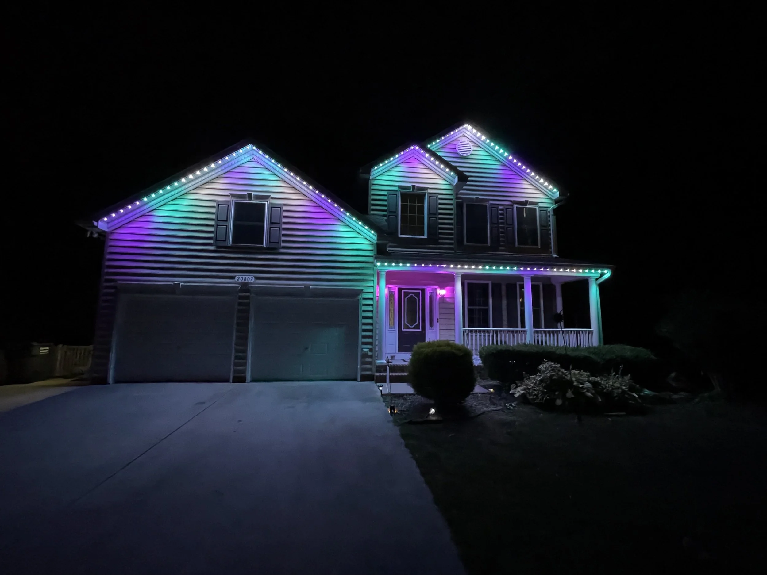A two-story house decorated with colorful Christmas lights at night, with a dark sky in the background.