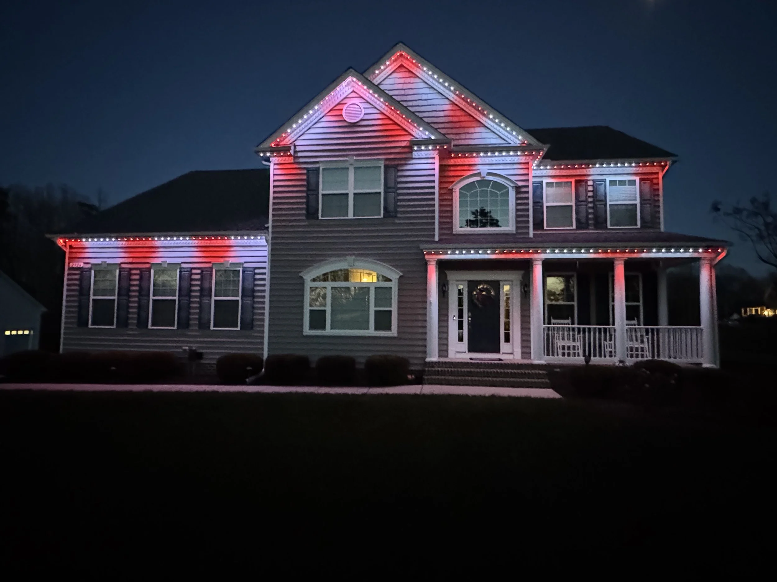 A two-story house decorated with red, white, and blue string lights at night.