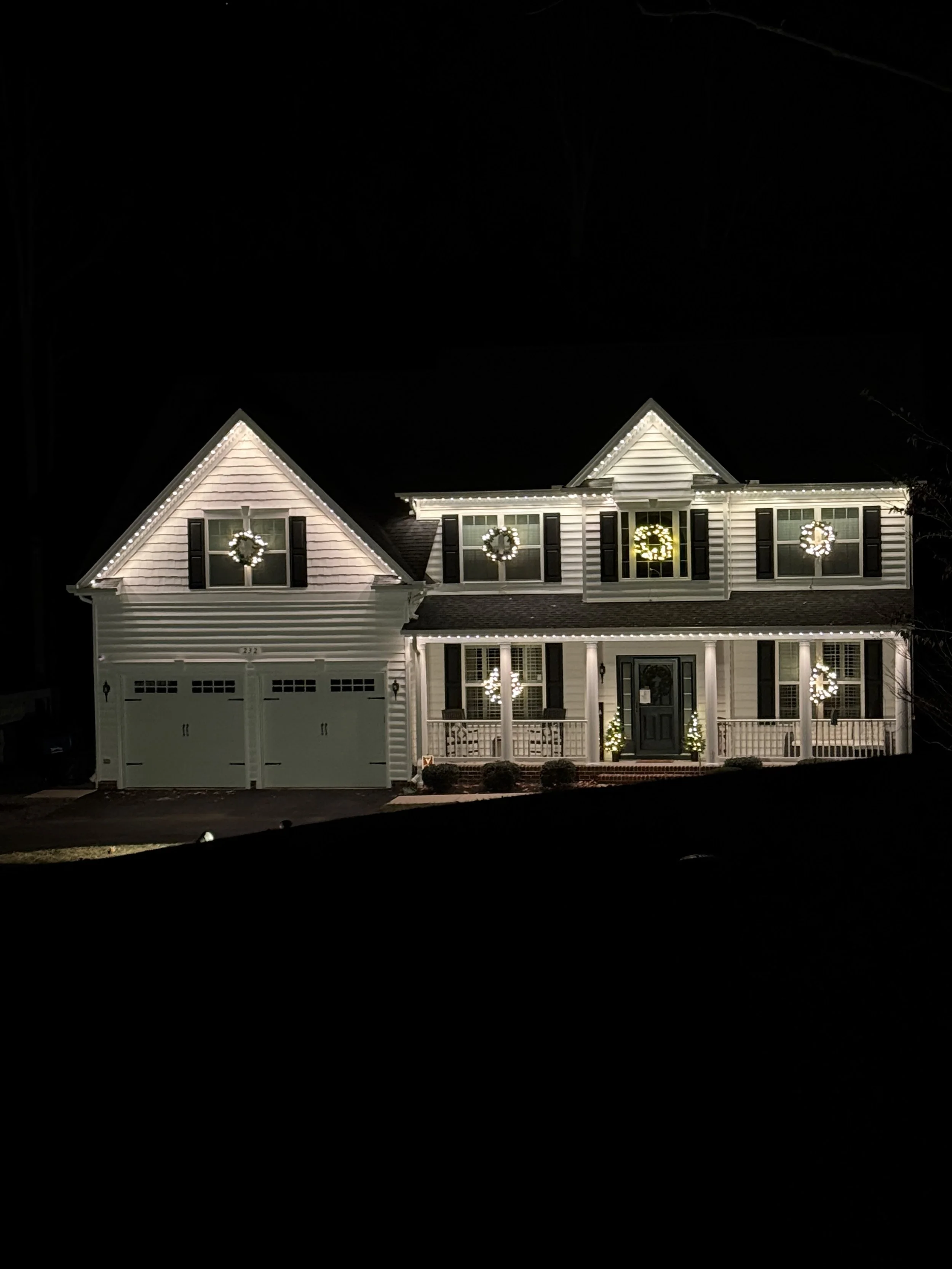 A two-story house decorated with Christmas wreaths and lights at night.