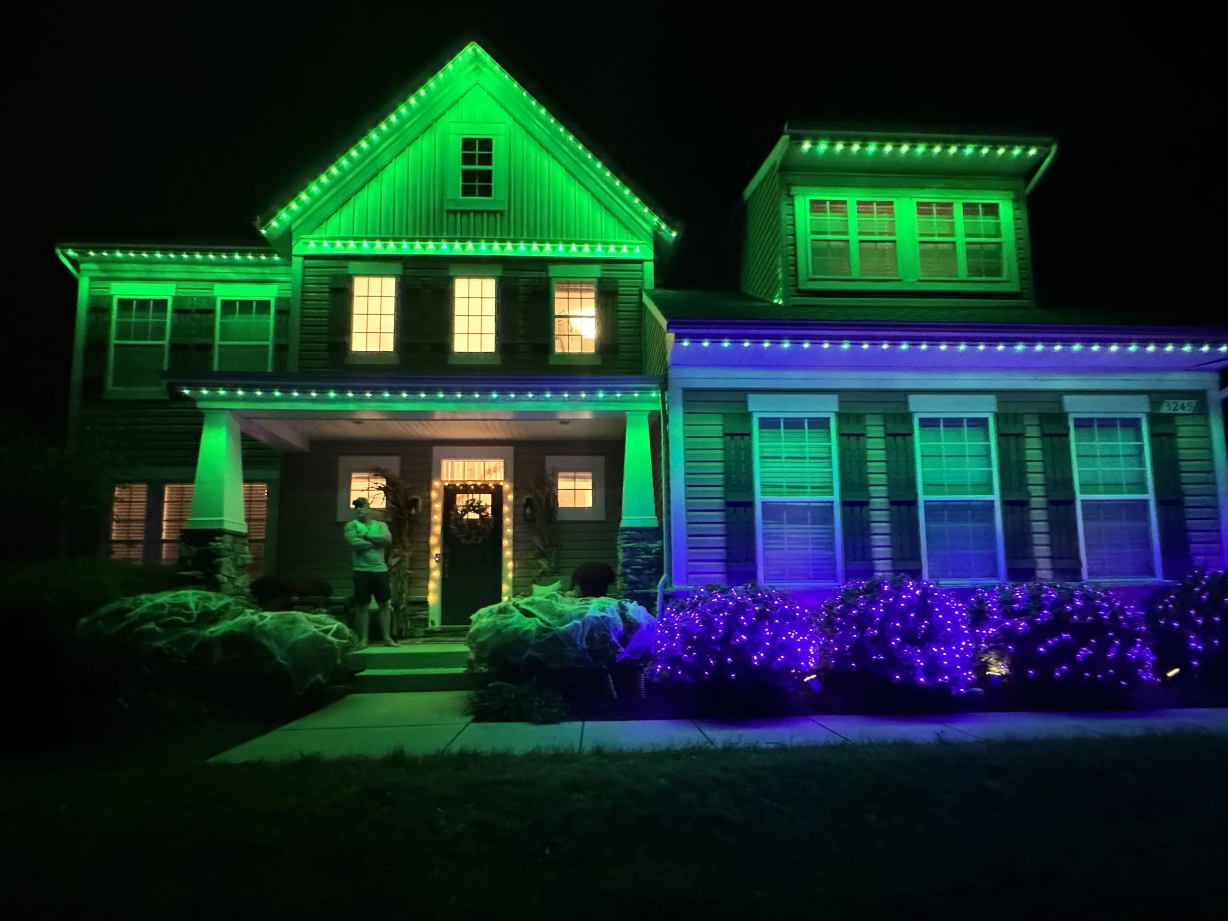 A house decorated with green and purple holiday lights at night.