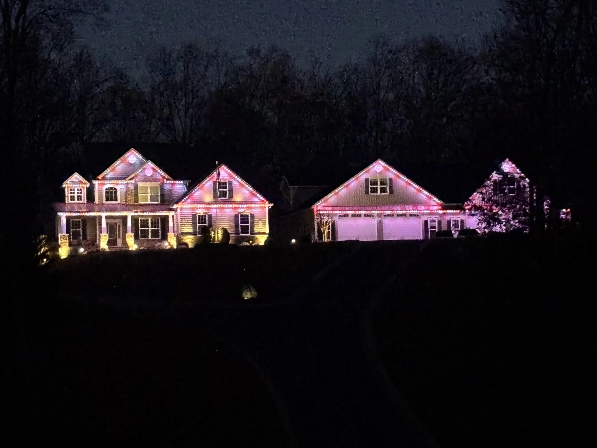 A large house decorated with pink and white Christmas lights at night, with trees in the background.