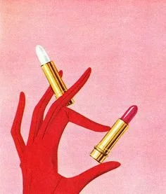 A hand wearing a red glove holding a lipstick designed to look like a lipstick tube, with the cap removed to reveal the pink lipstick inside, against a pink background.