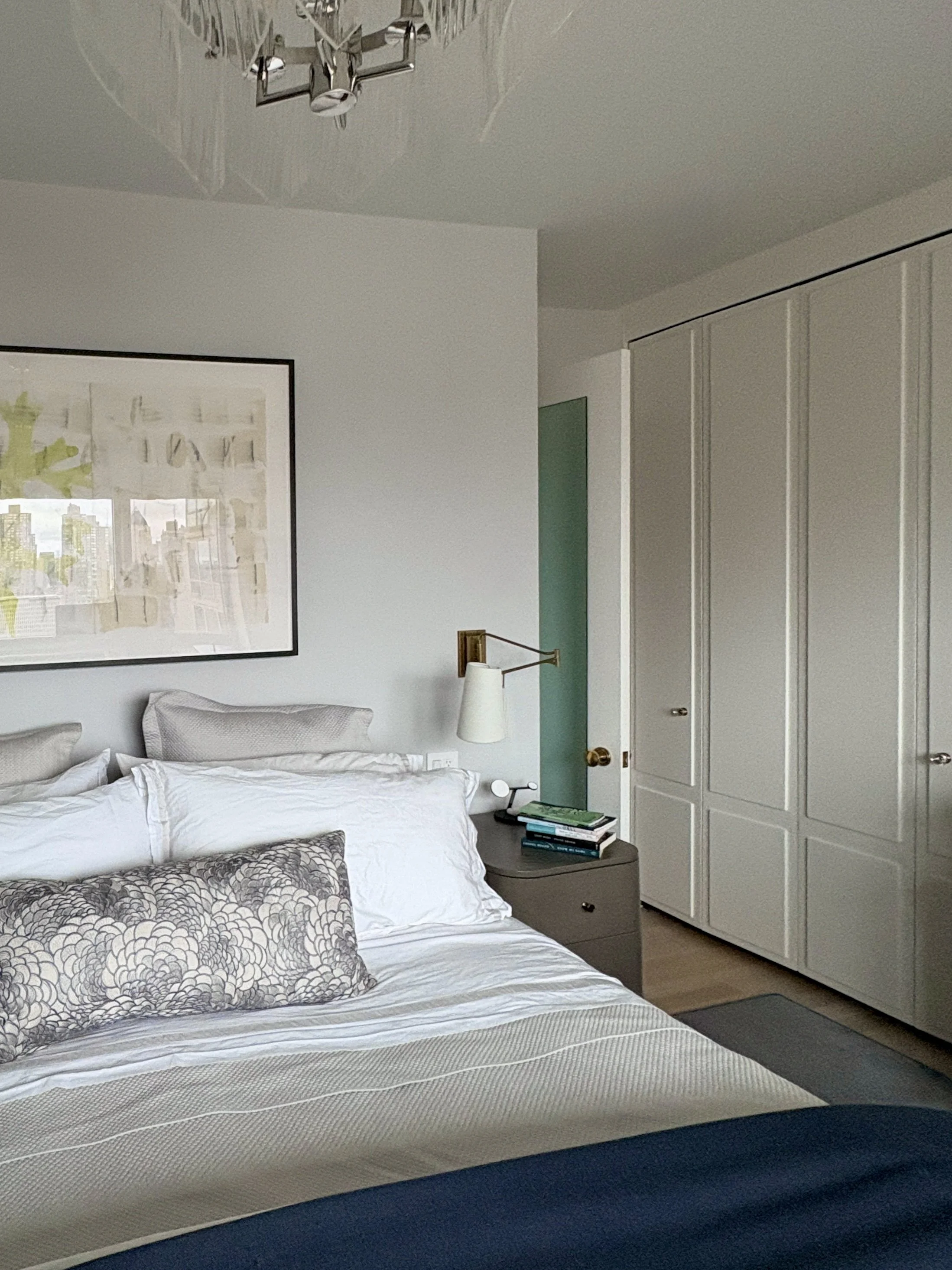 Upper West Side bedroom with custom panel-front closets, soft neutral bedding, brass swing-arm wall sconces, abstract artwork, and tailored millwork creating a warm modern mid-century retreat in a Manhattan apartment.