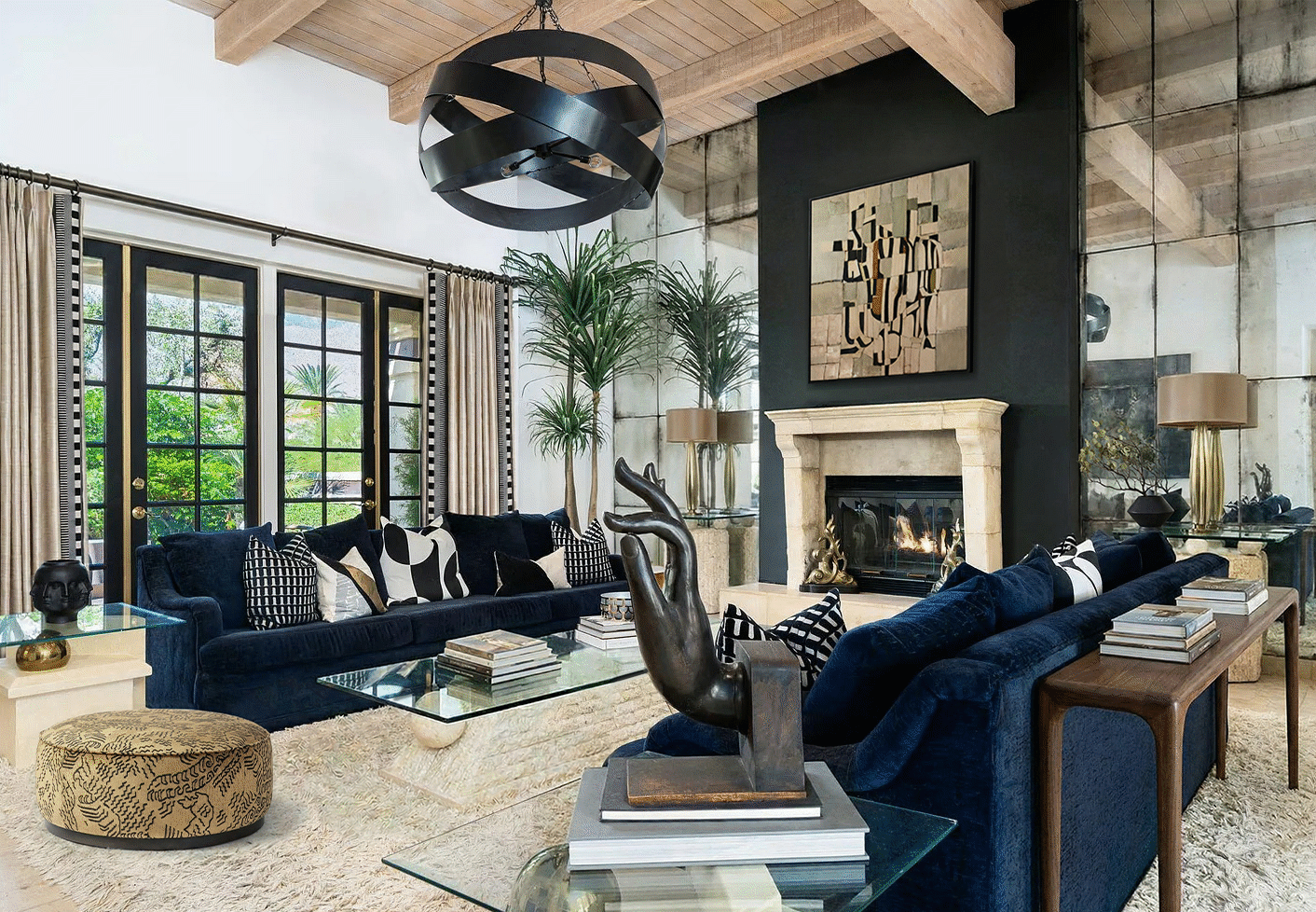Palm Springs living room with navy velvet sofas, sculptural black chandelier, exposed wood beams, dramatic dark fireplace wall, mirrored panels, and mid-century modern desert styling.