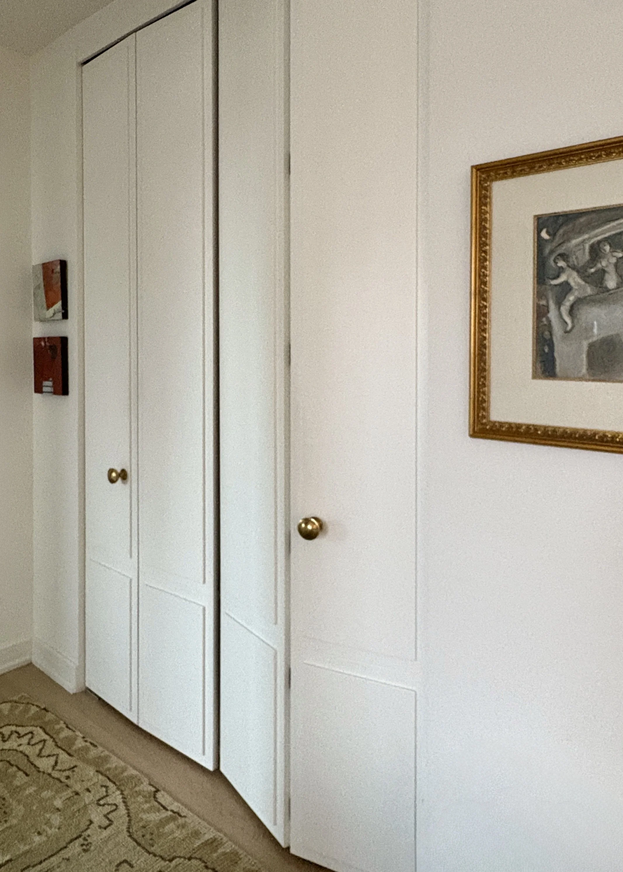 Custom Upper West Side millwork closet featuring modern shaker-style white cabinetry, burnished brass Katonah hardware, and vintage kilim carpet.