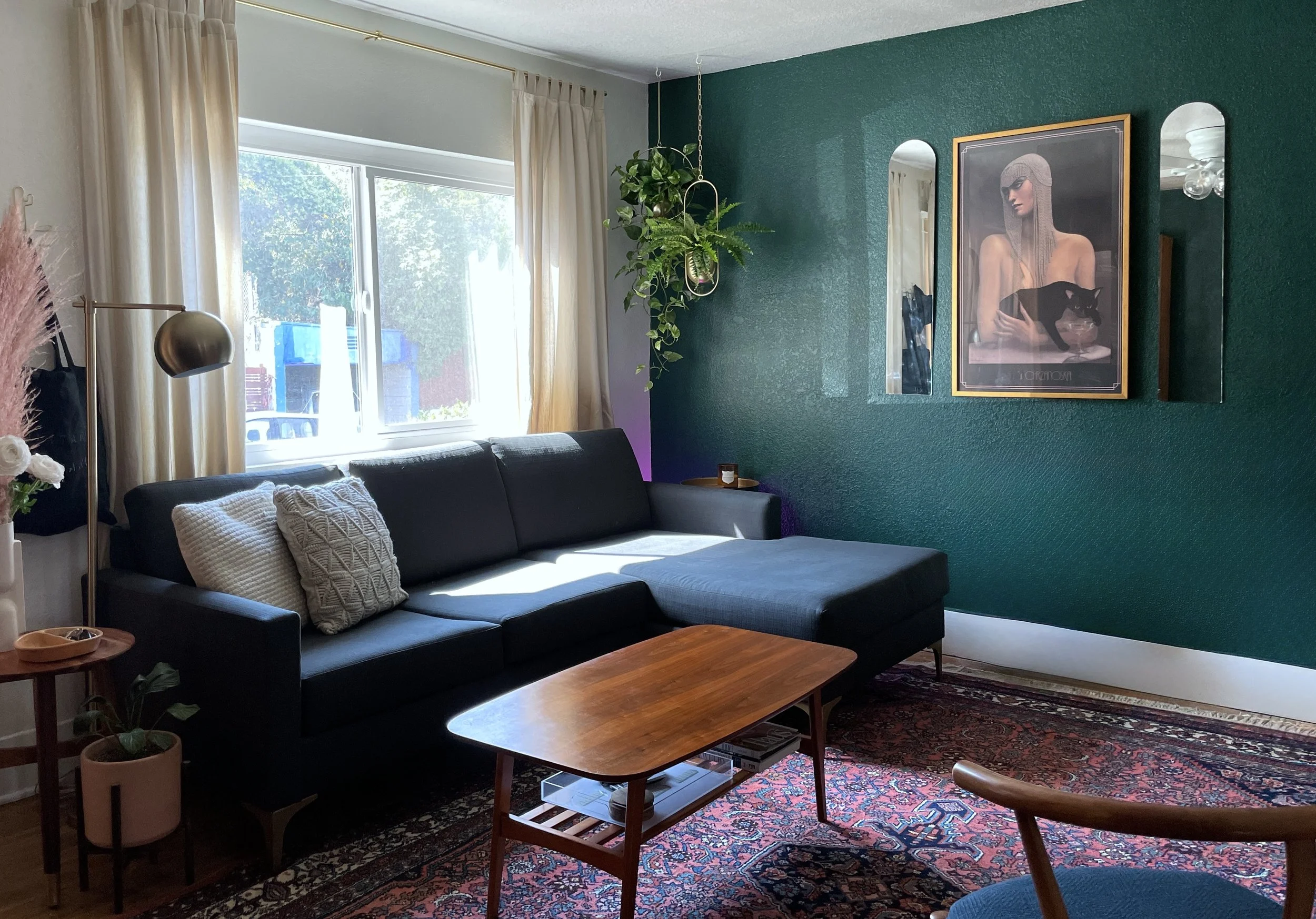 Echo Park bungalow living room featuring deep green statement wall, navy sectional sofa, vintage Persian rug with rust and indigo tones, mid-century coffee table, hanging planter, layered artwork, and eclectic vintage-modern styling in Los Angeles.