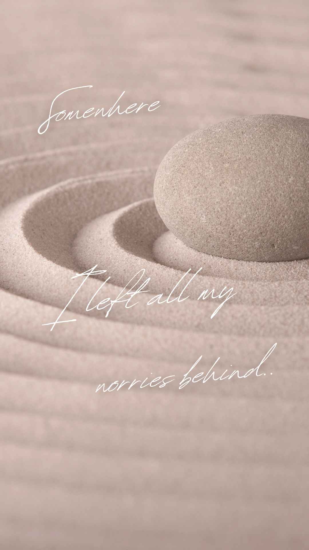 A smooth gray stone resting on sand with concentric patterns, with the words "somewhere left all my worries behind" overlayed in white cursive font.