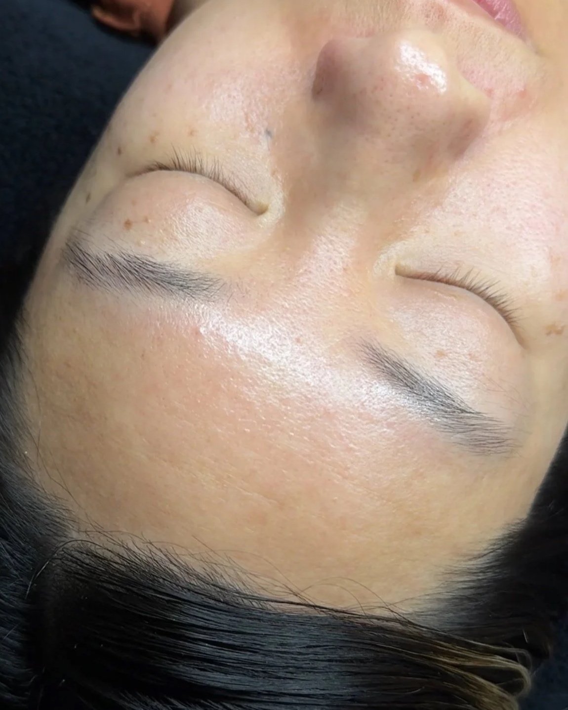 Close-up of a person's face with smooth, clear skin, closed eyes, and well-groomed eyebrows.