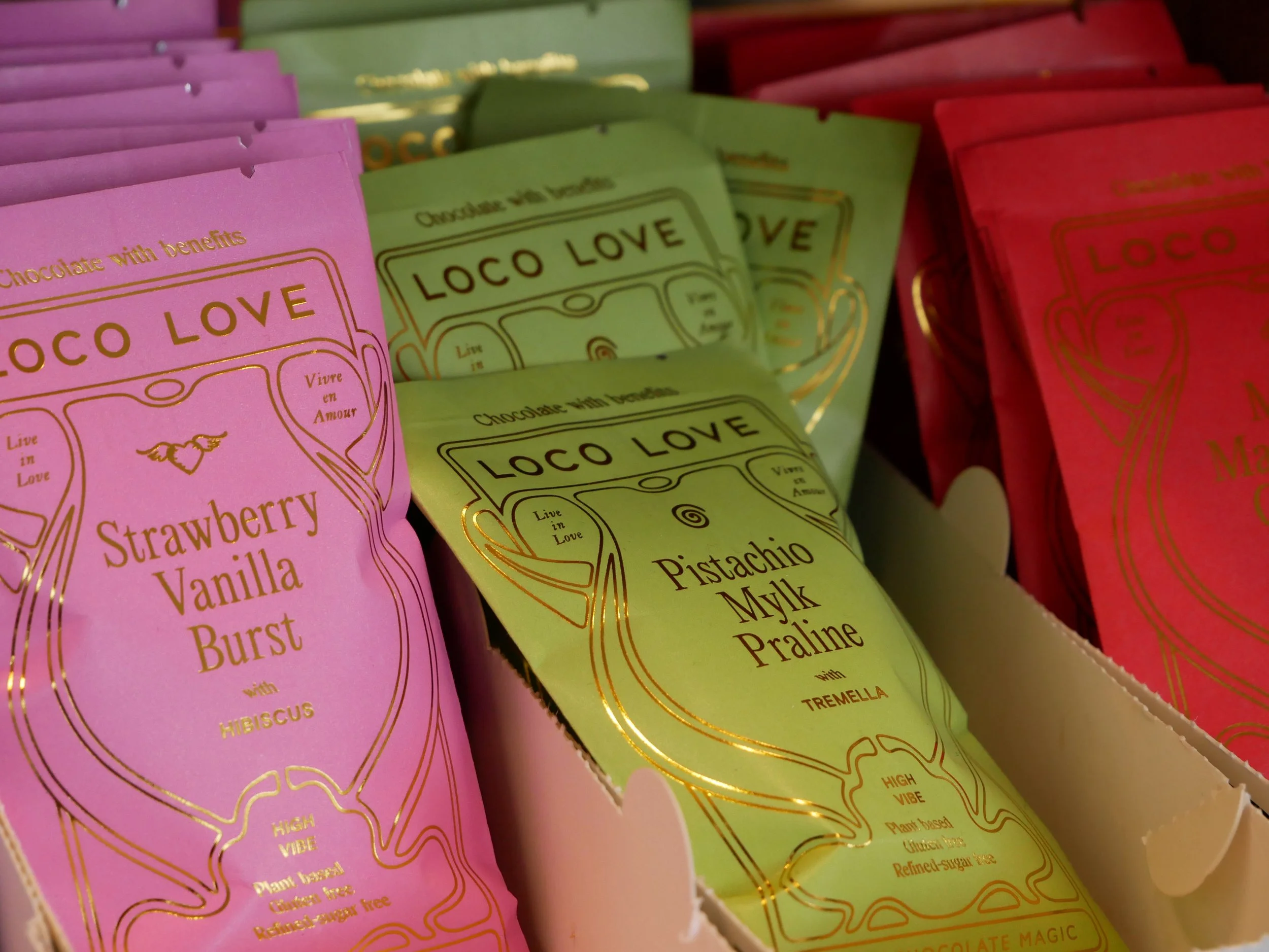 Multicolored snack bars with gold foil packaging labeled 'Loco Love,' featuring flavors like strawberry vanilla, pistachio milk, and strawberry cheesecake, arranged on a display.