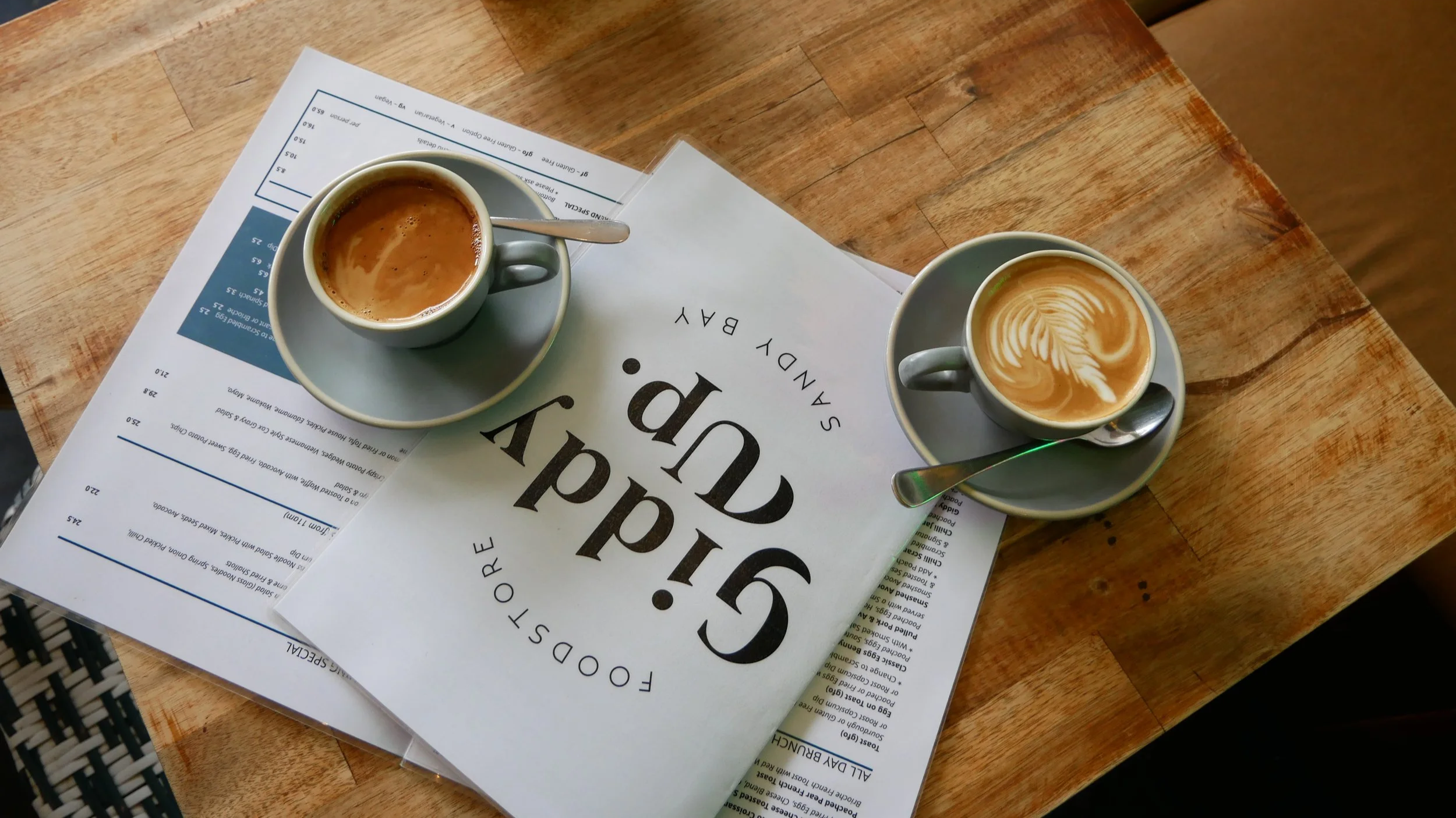 Two cups of coffee with latte art on a wooden table, placed on top of menus and restaurant papers.