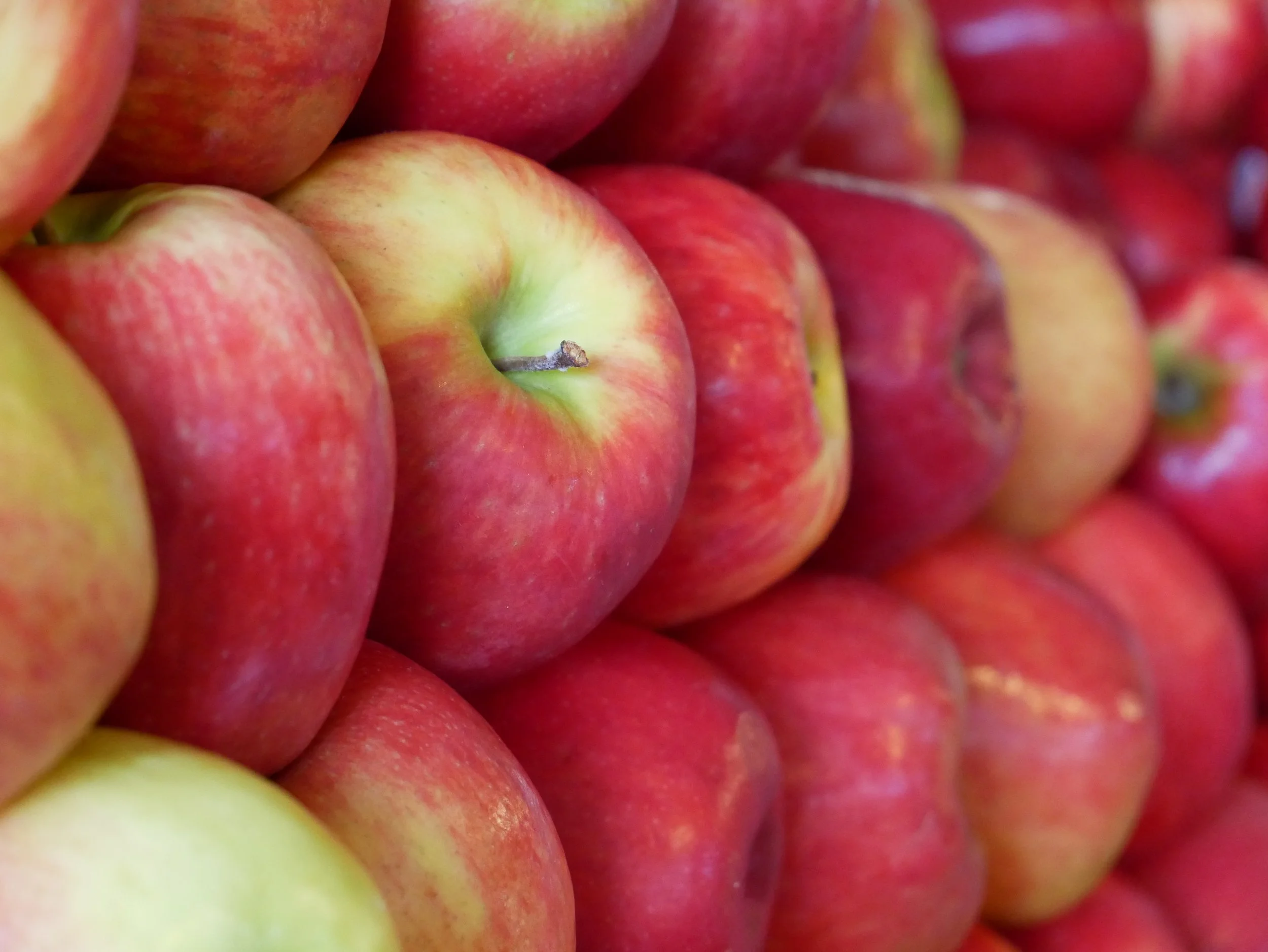 Close-up of multiple fresh red and yellow apples stacked together.
