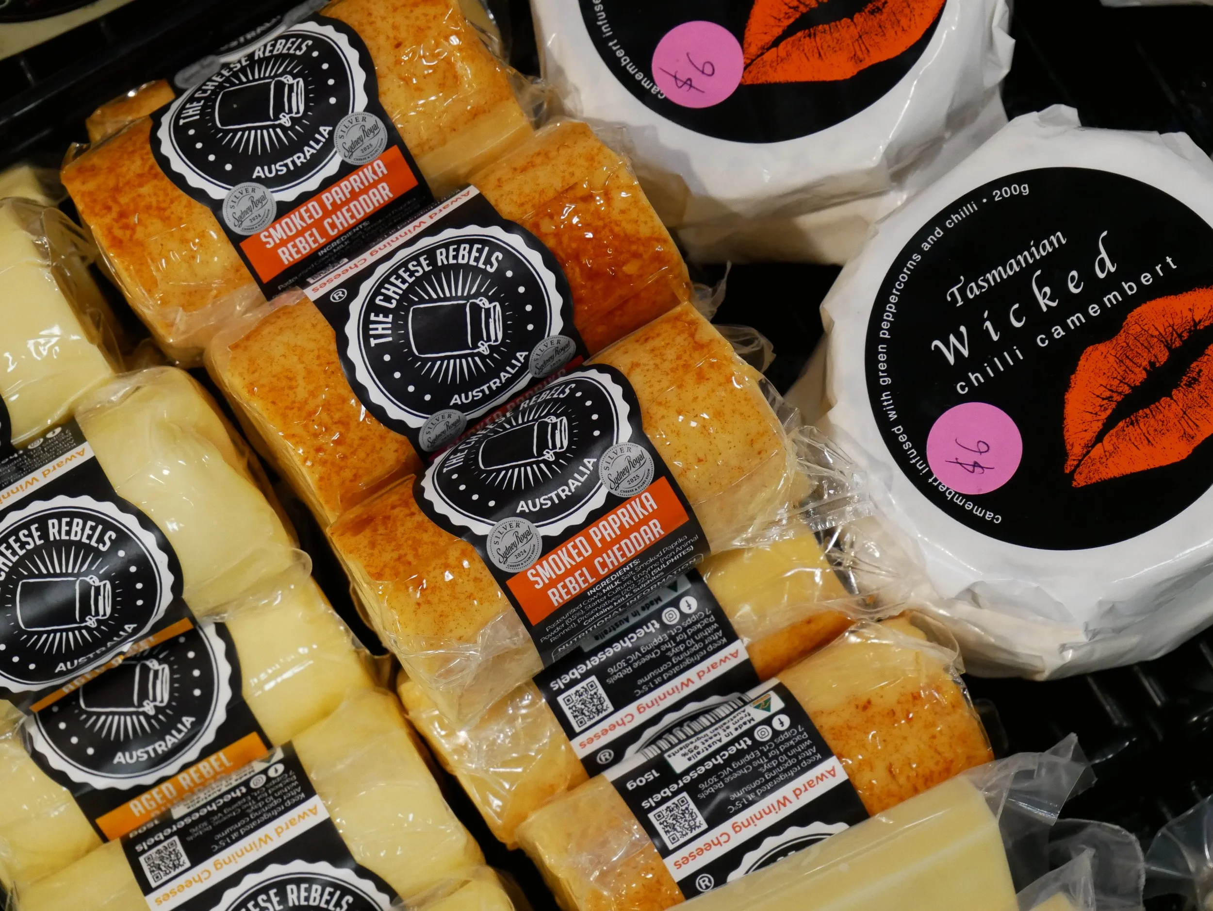 Packages of cheese labeled as smoked paprika rebel cheddar and aged white cheddar in a grocery store display.