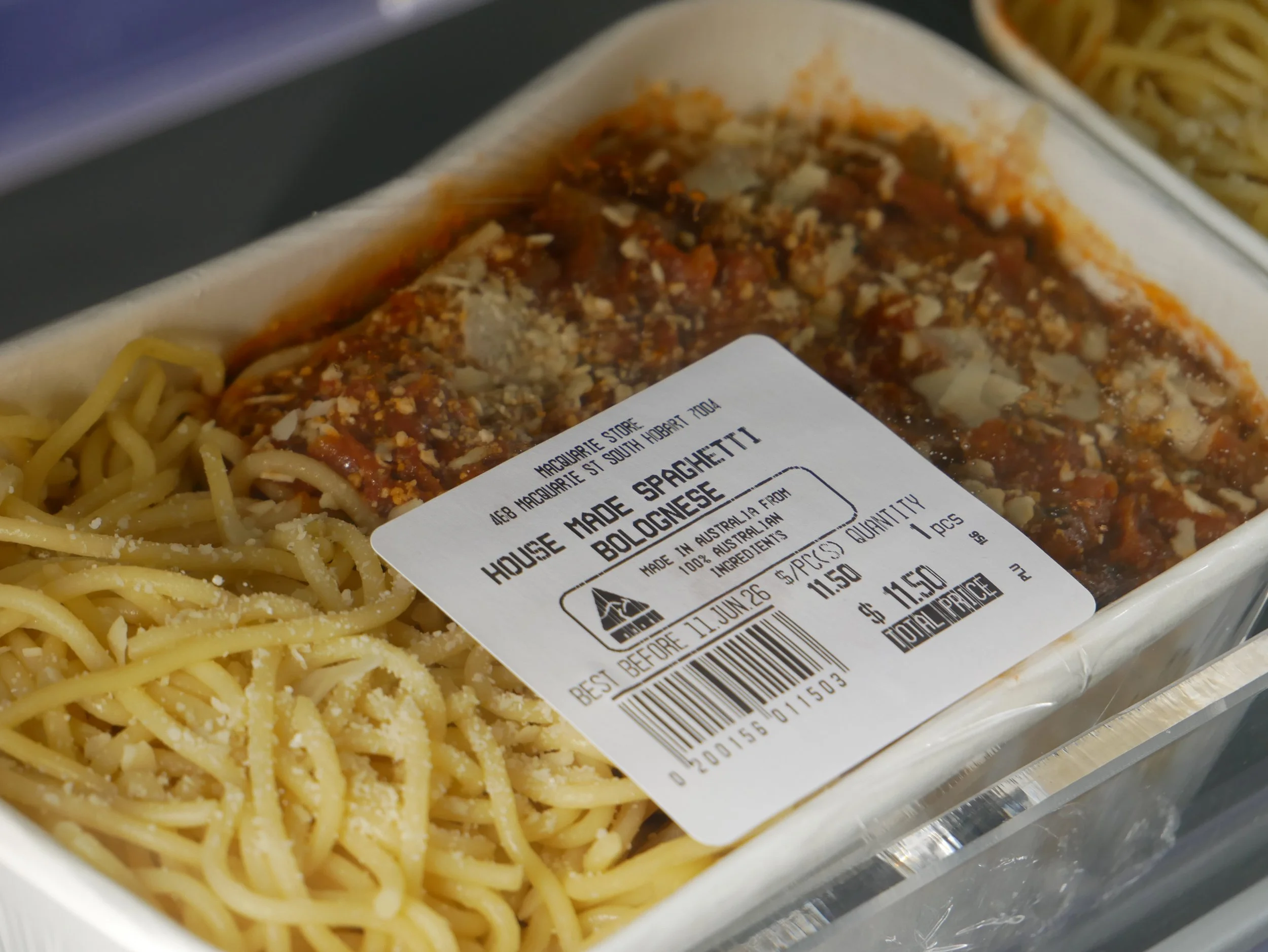 Pre-packaged spaghetti with meat sauce in a plastic container, with a partial label showing details about the product, including its name and ingredients.