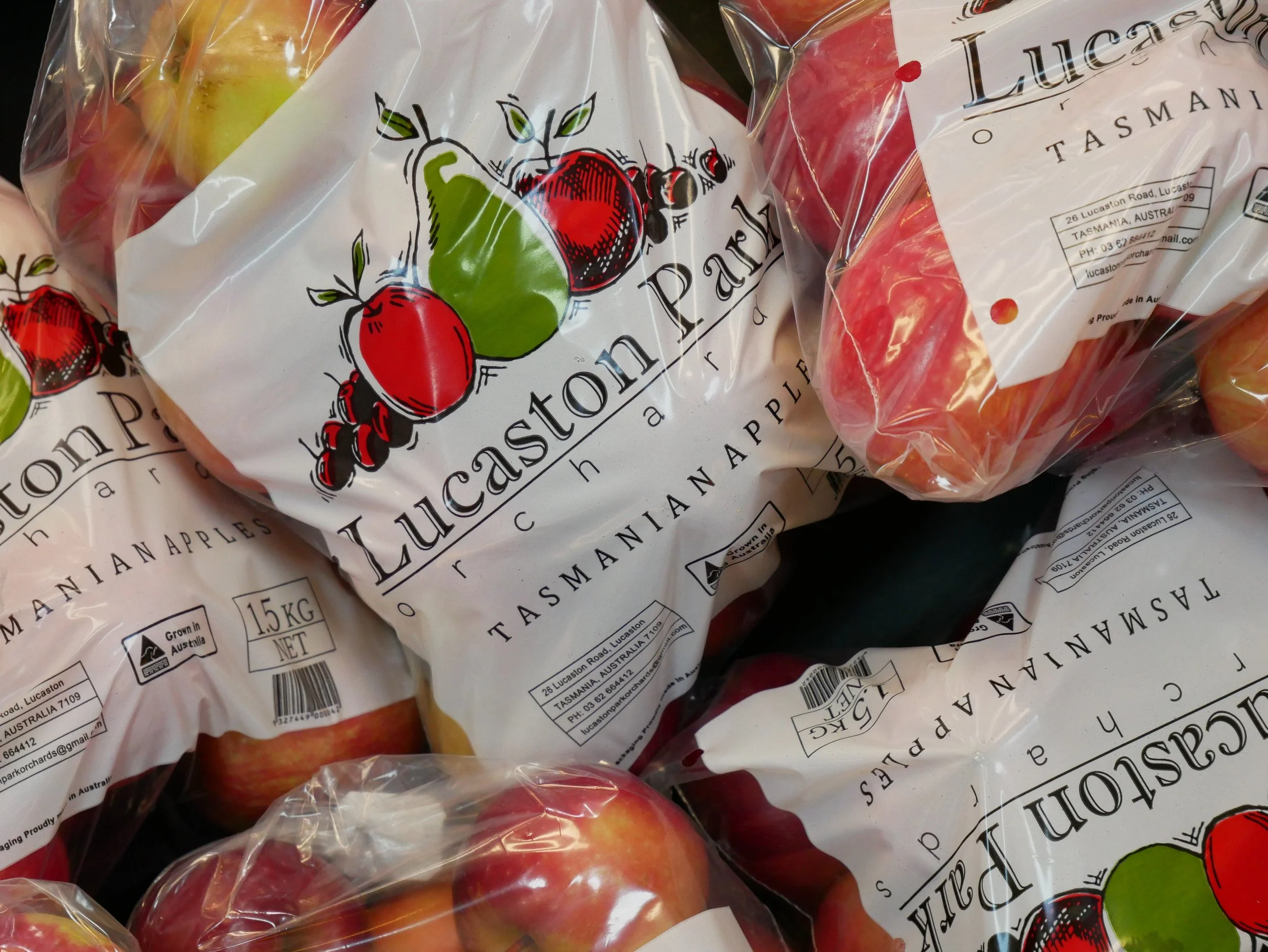 Bags of apples with a label that reads 'Lucaston Apples Tasmanian,' showing red and yellow apples inside clear plastic packaging.