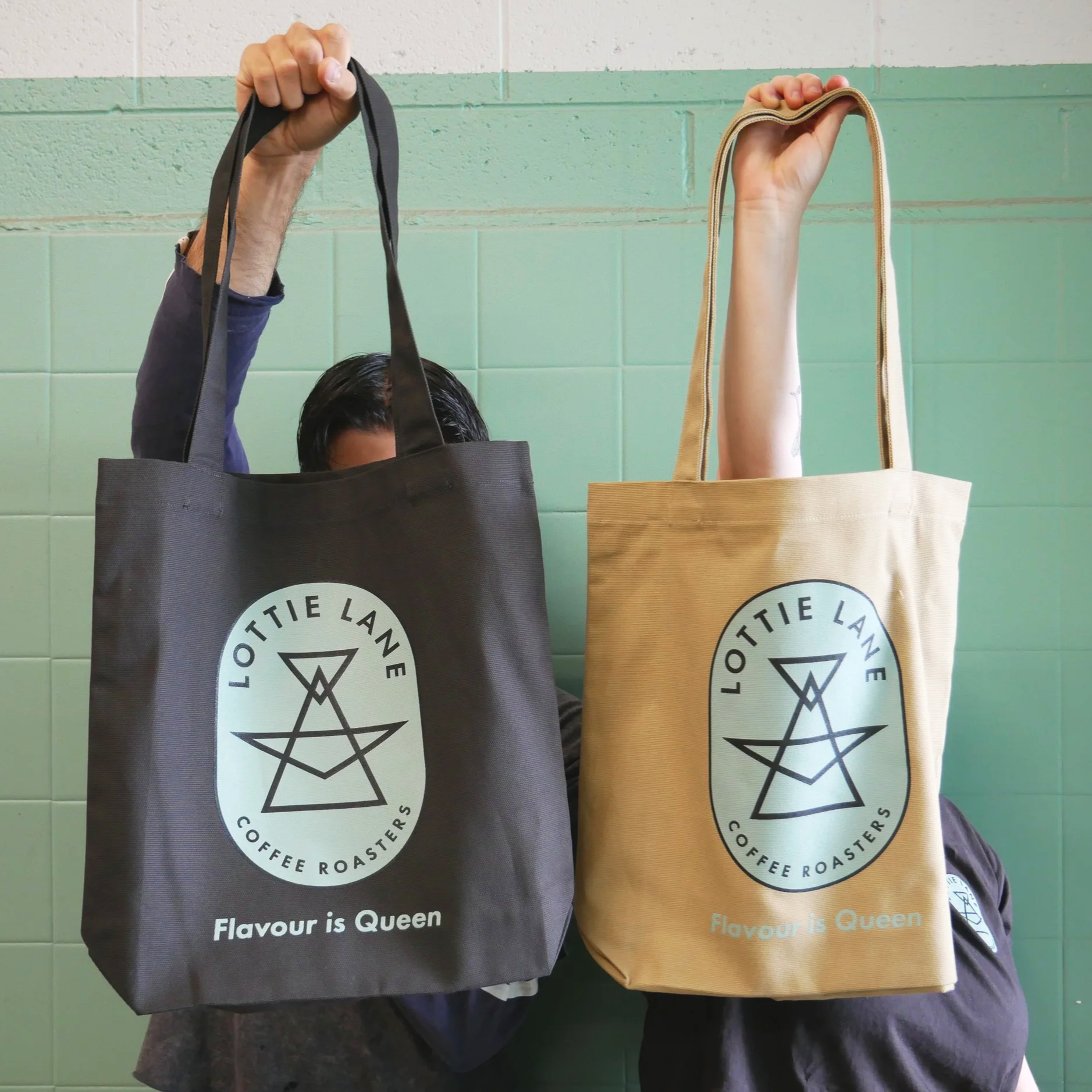 Two people holding tote bags against a teal green background.
