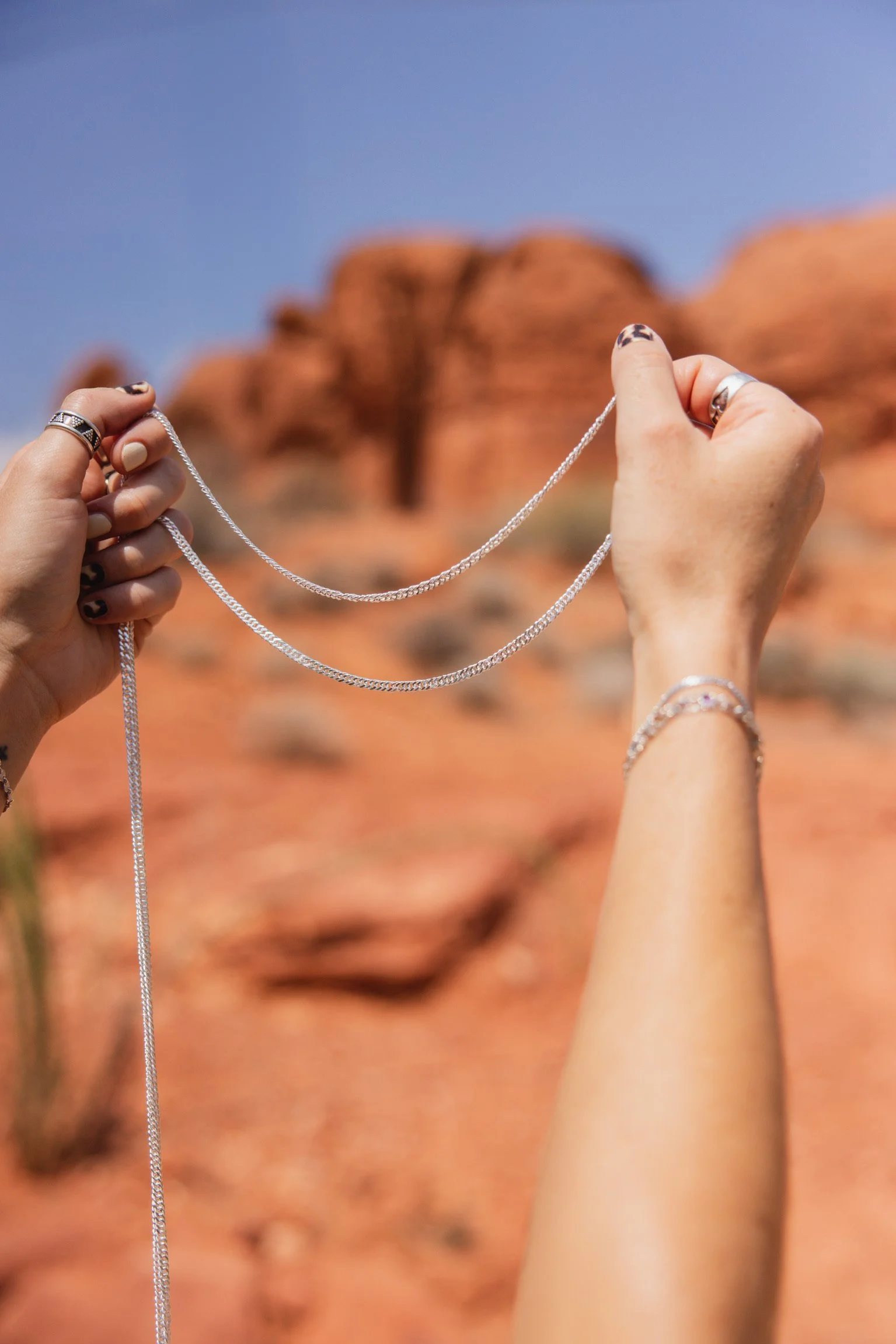 Permanent jewelry chains held up in front of red cliffs in St. George