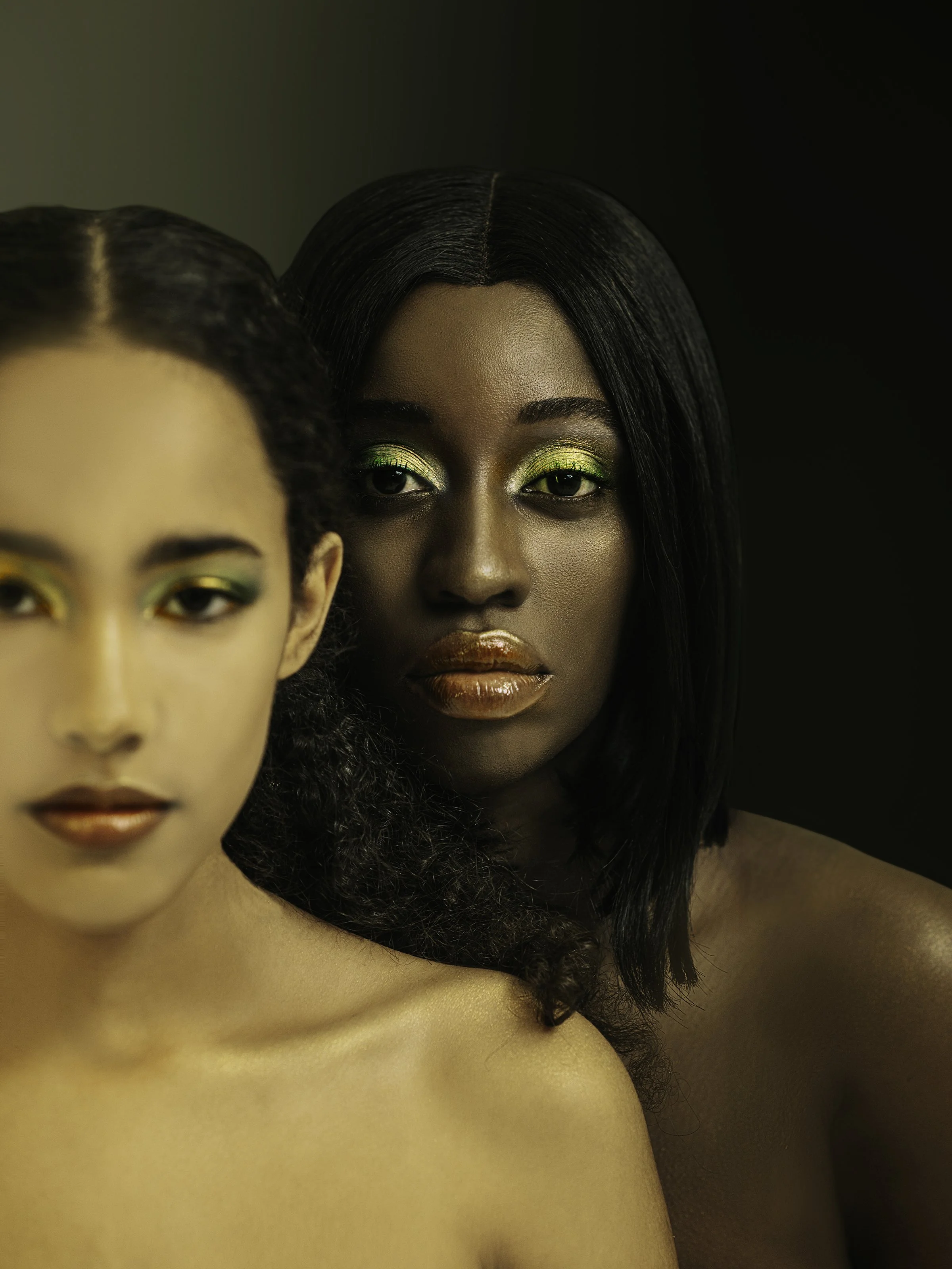 Close-up of two women with bold makeup and dark clothing in a studio portrait.