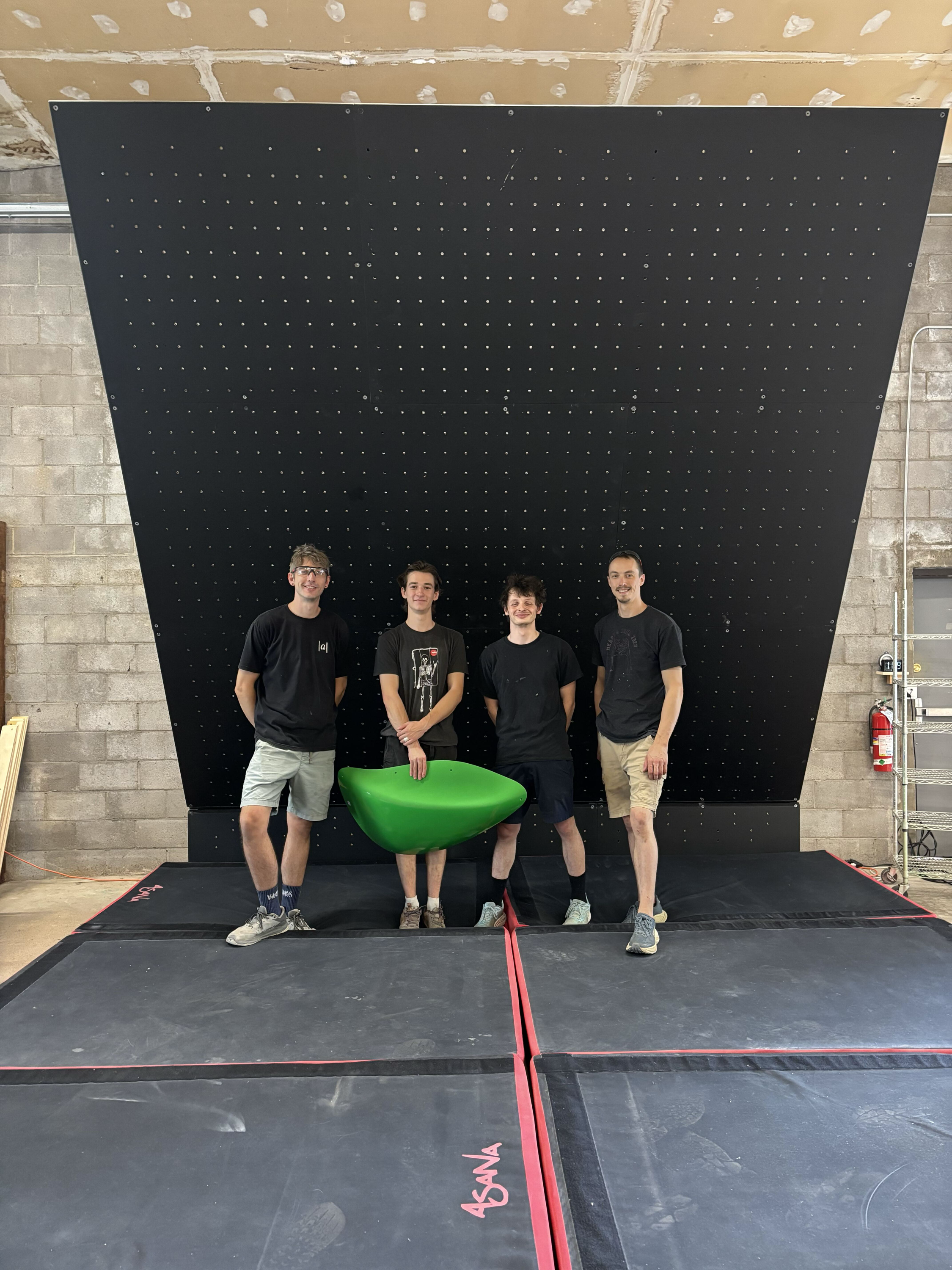 Four members of the Absolute team holding a green climbing macro in the workshop