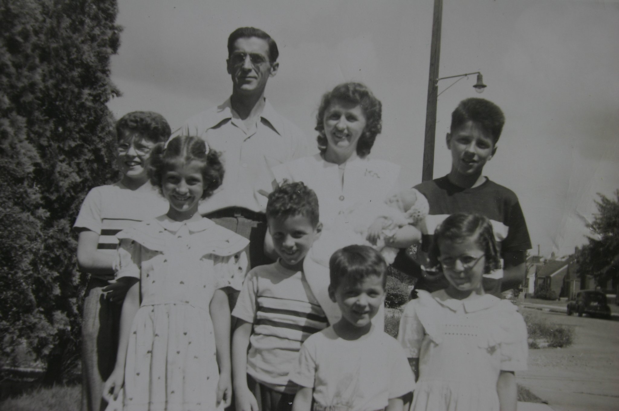 A black and white photo of a family in 1949 featuring two adults, six children, and a baby being held