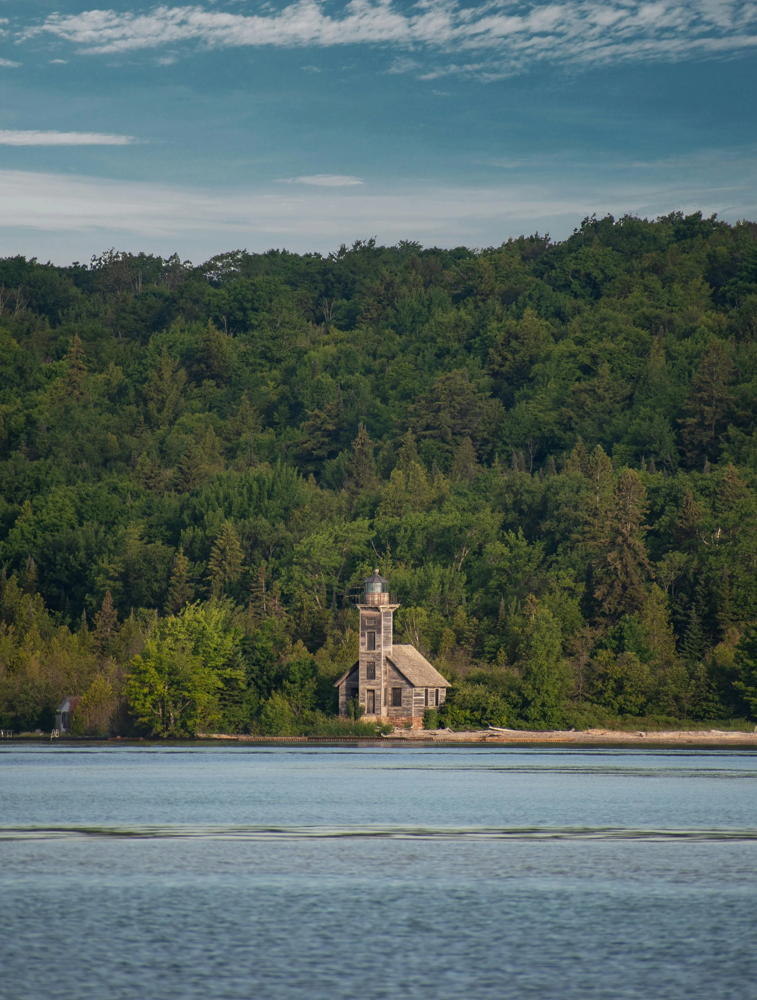 worn wooden lighthouse sits on the shores of a lake with a forest behind it