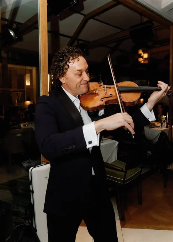 A man in a black tuxedo playing a violin in a restaurant.