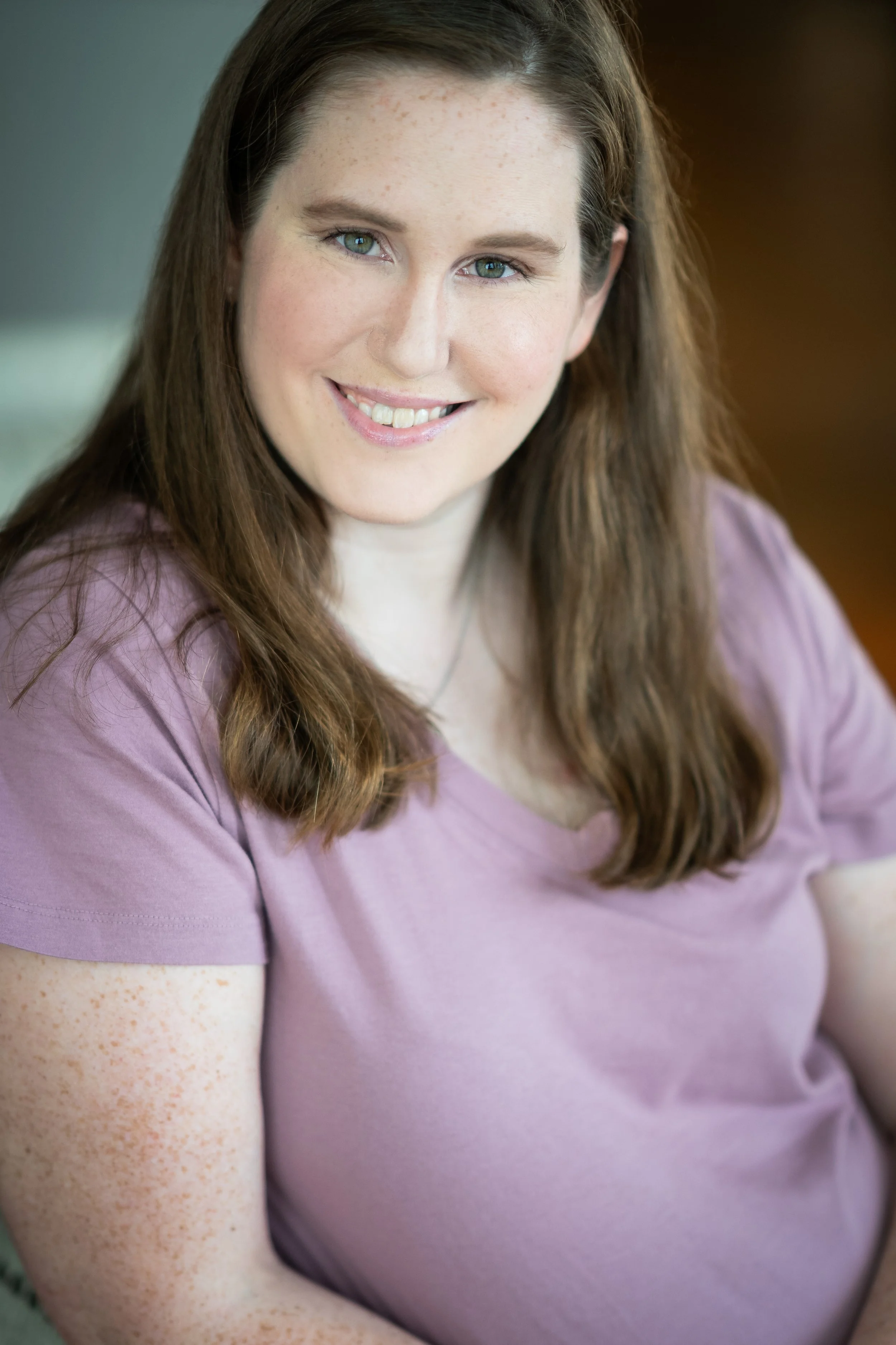 A woman with long brown hair and freckles, smiling and wearing a purple shirt.