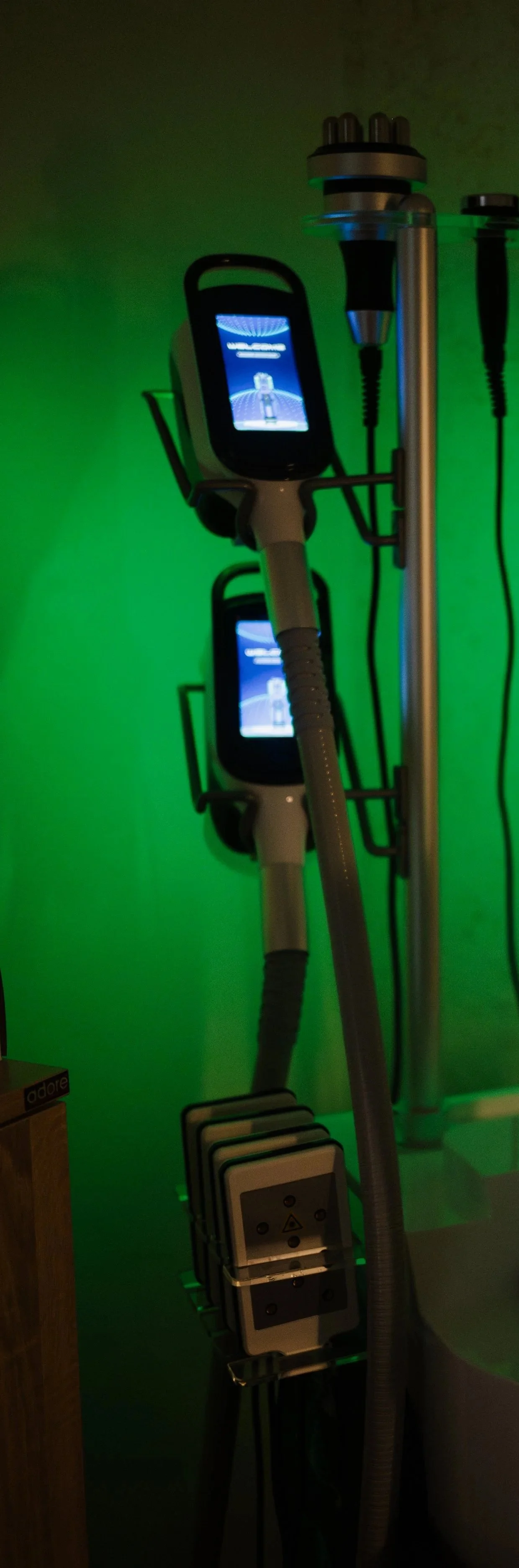 Medical or aesthetic device with two screens, positioned on a stand against a green background, likely used for treatment or diagnostics.