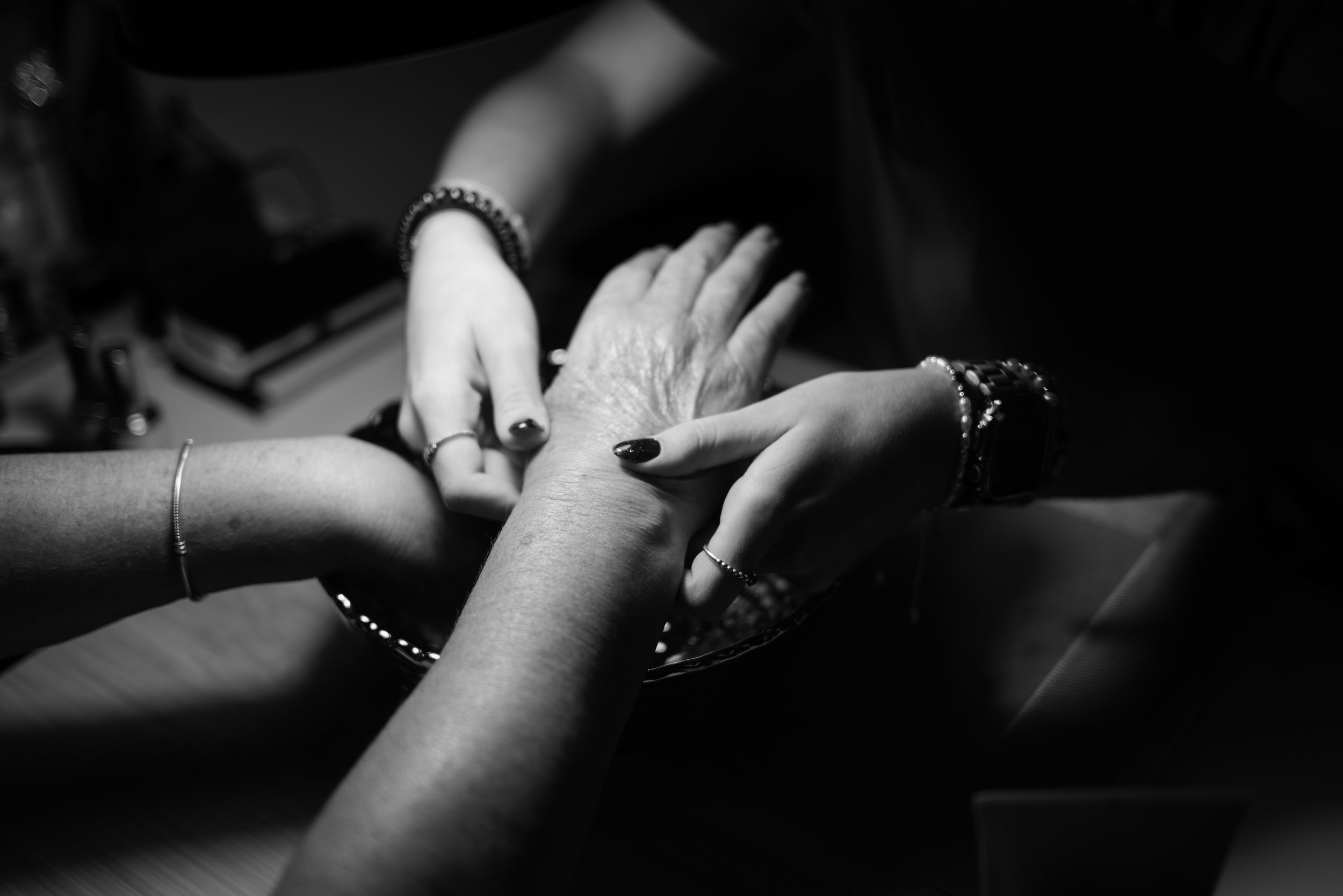 A black and white photo of three hands, with two younger hands touching an older person's hand, symbolizing care or support.