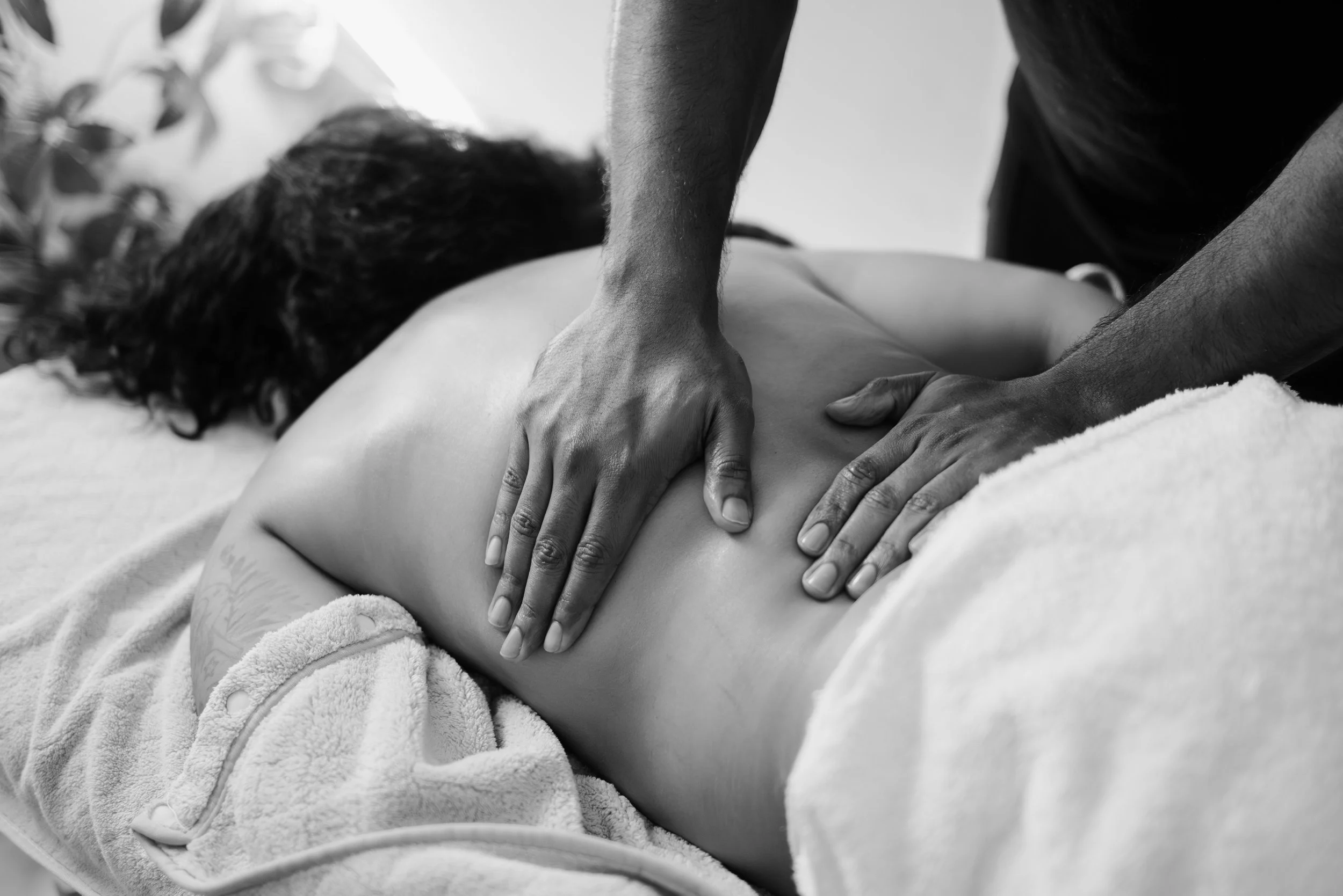A person receiving a back massage from a massage therapist, lying face down on a massage table, with the therapist applying pressure with both hands.