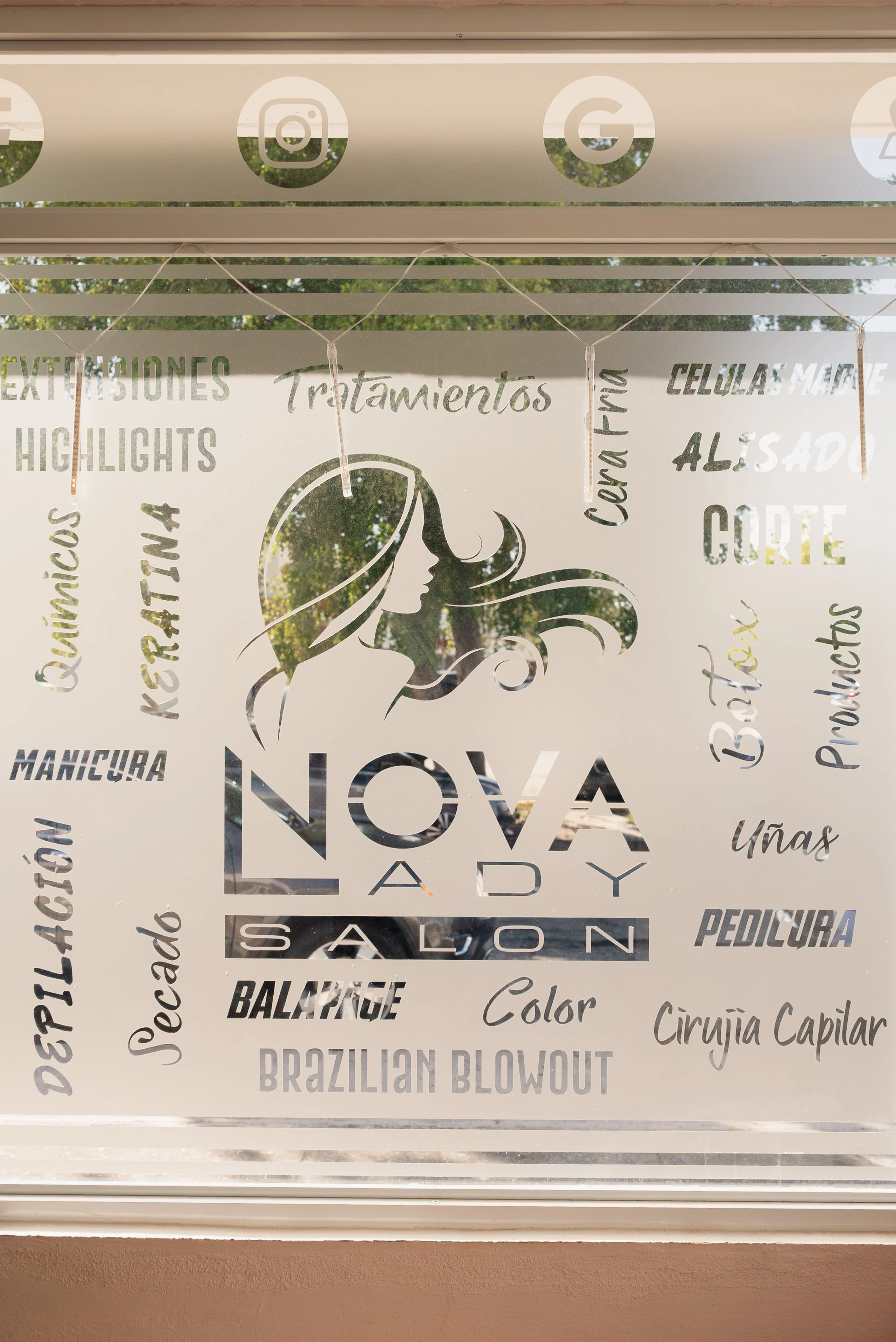 A window decal for Nova Lady Salon featuring a stylized profile of a woman with flowing hair, surrounded by words in Spanish related to beauty services such as treatments, highlights, treatments, eyebrows, manicure, pedicure, coloring, haircuts, and capillary surgery.