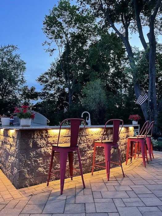 Outdoor kitchen illuminated with under-counter hardscape lights and ambient lighting for a perfect mood ambiance.