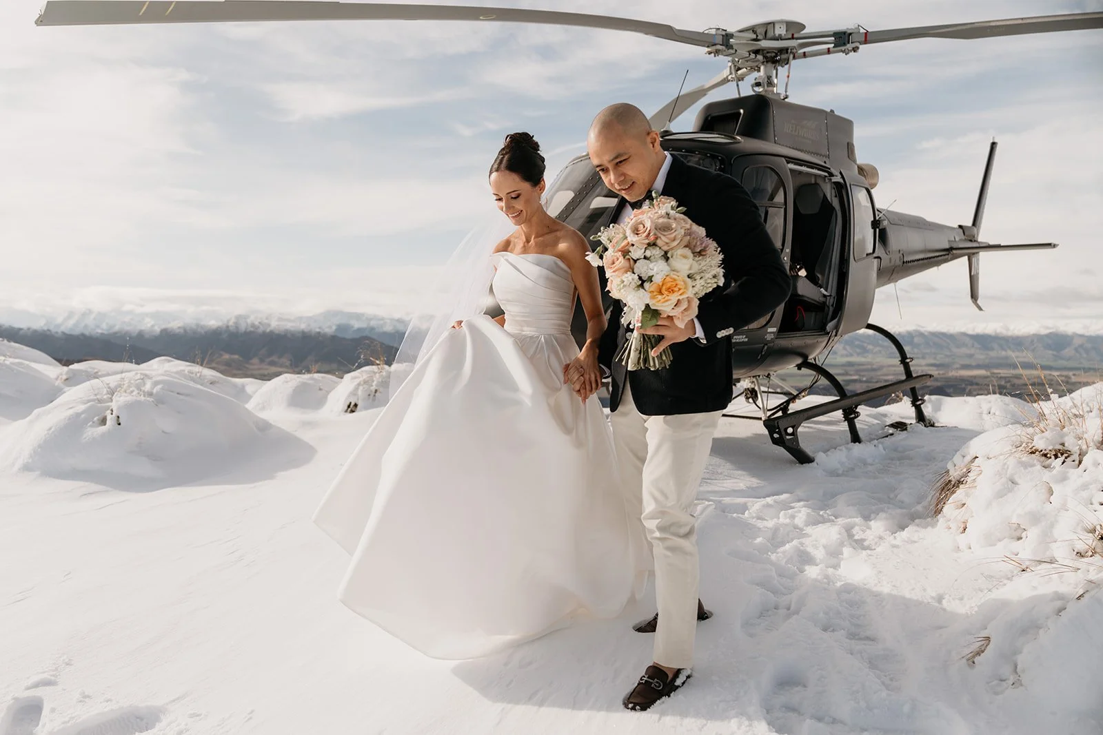 Bride and groom in snow with a helicopter